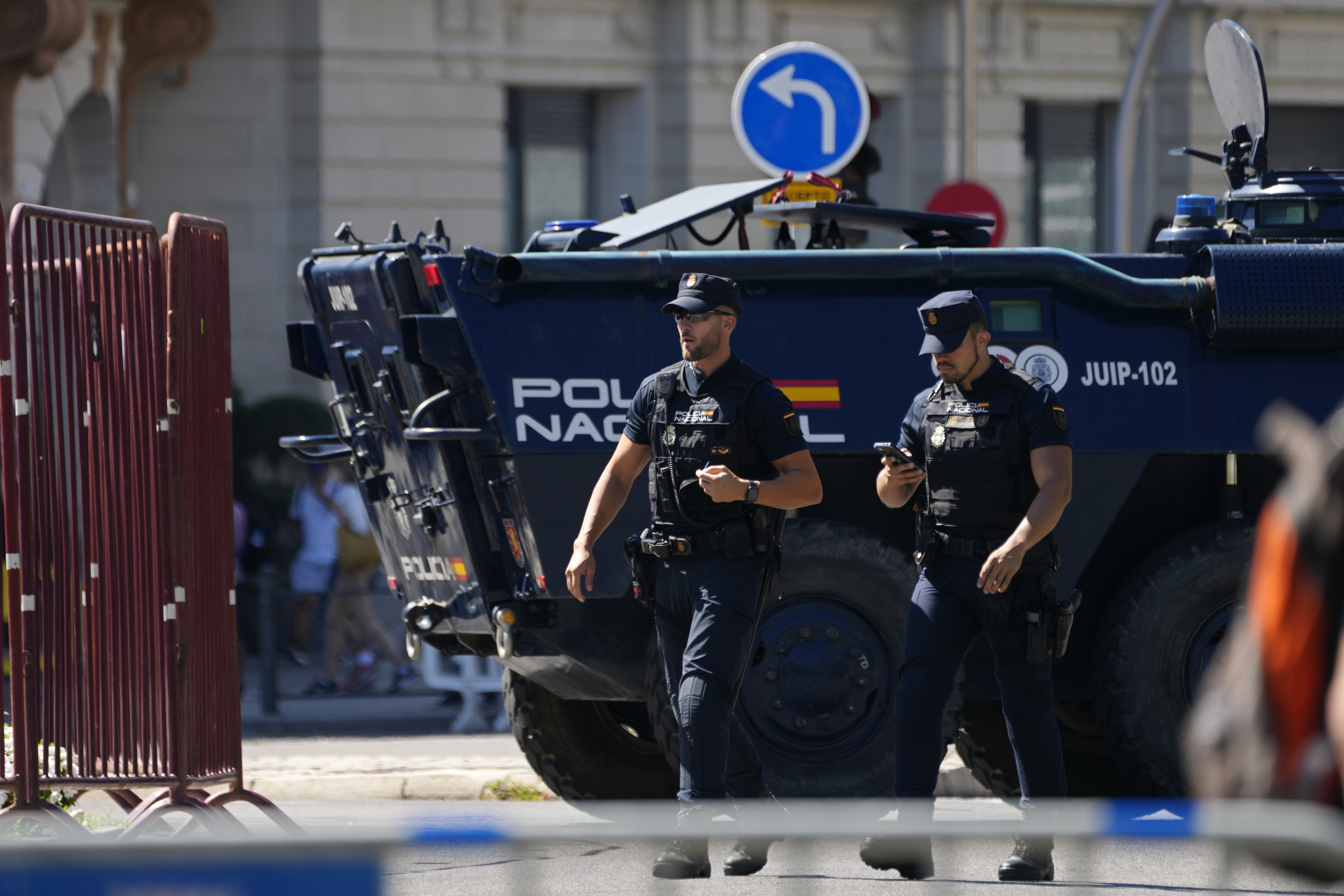 Police officers walk by a police armoured vehicle before the last stage of La Vuelta cycling race in Madrid, Spain, Sunday, Sept. 8, 2024.
