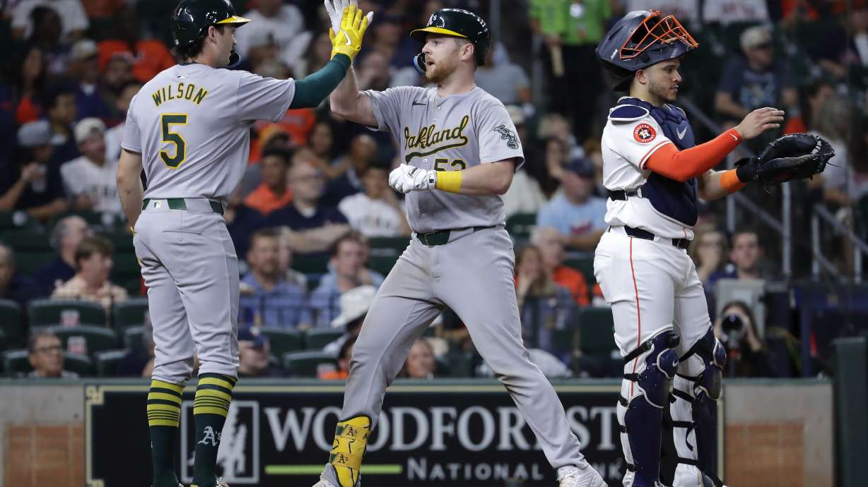 Oakland Athletics' Jacob Wilson (5) and Kyle McCann, center, celebrate next to Houston Astros catcher Yainer Diaz, right, after they both scored on the two-run home run by McCann during the sixth inning of a baseball game, Wednesday, Sept. 11, 2024, in Houston.