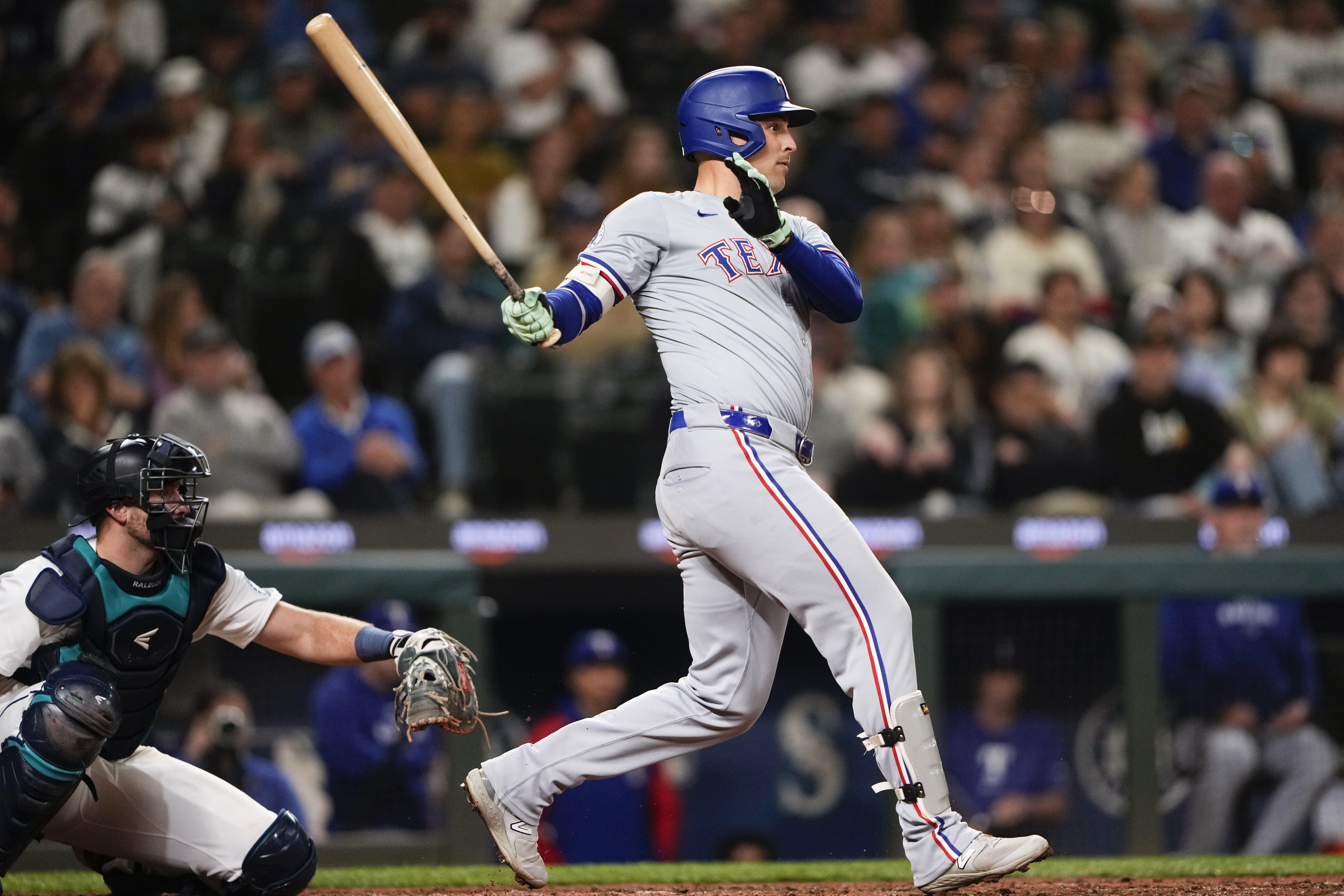 Texas Rangers' Nathaniel Lowe follows through on an RBI single to score Wyatt Langford as Seattle Mariners catcher Cal Raleigh looks on during the eighth inning of a baseball game Thursday, Sept. 12, 2024, in Seattle.