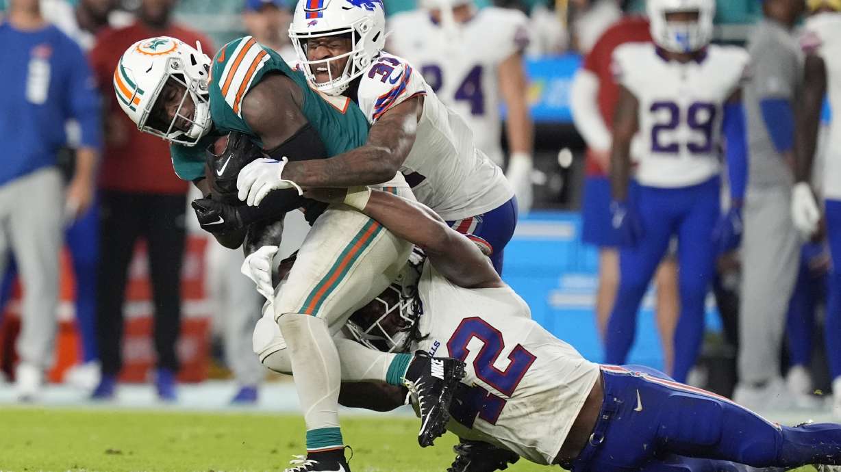 Miami Dolphins running back De'Von Achane is tackled by Buffalo Bills linebacker Dorian Williams (42) and cornerback Rasul Douglas (31) during the second half of an NFL football game, Thursday, Sept. 12, 2024, in Miami Gardens, Fla.