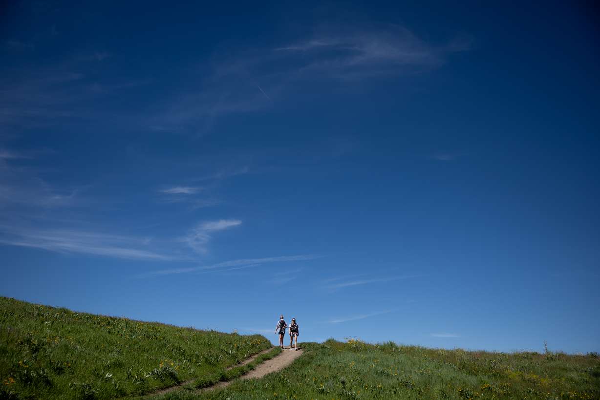 Riley Downs and her daughter, Alaina, 8 months, and Jeni Eyre and her son, Evan, 7 months, walk among green grasses in the foothills above Salt Lake City on June 2, 2022.