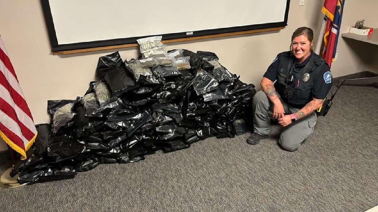 Helper police officer Lara Olson poses in front of over 80 pounds of marijuana seized at a DUI checkpoint Friday.