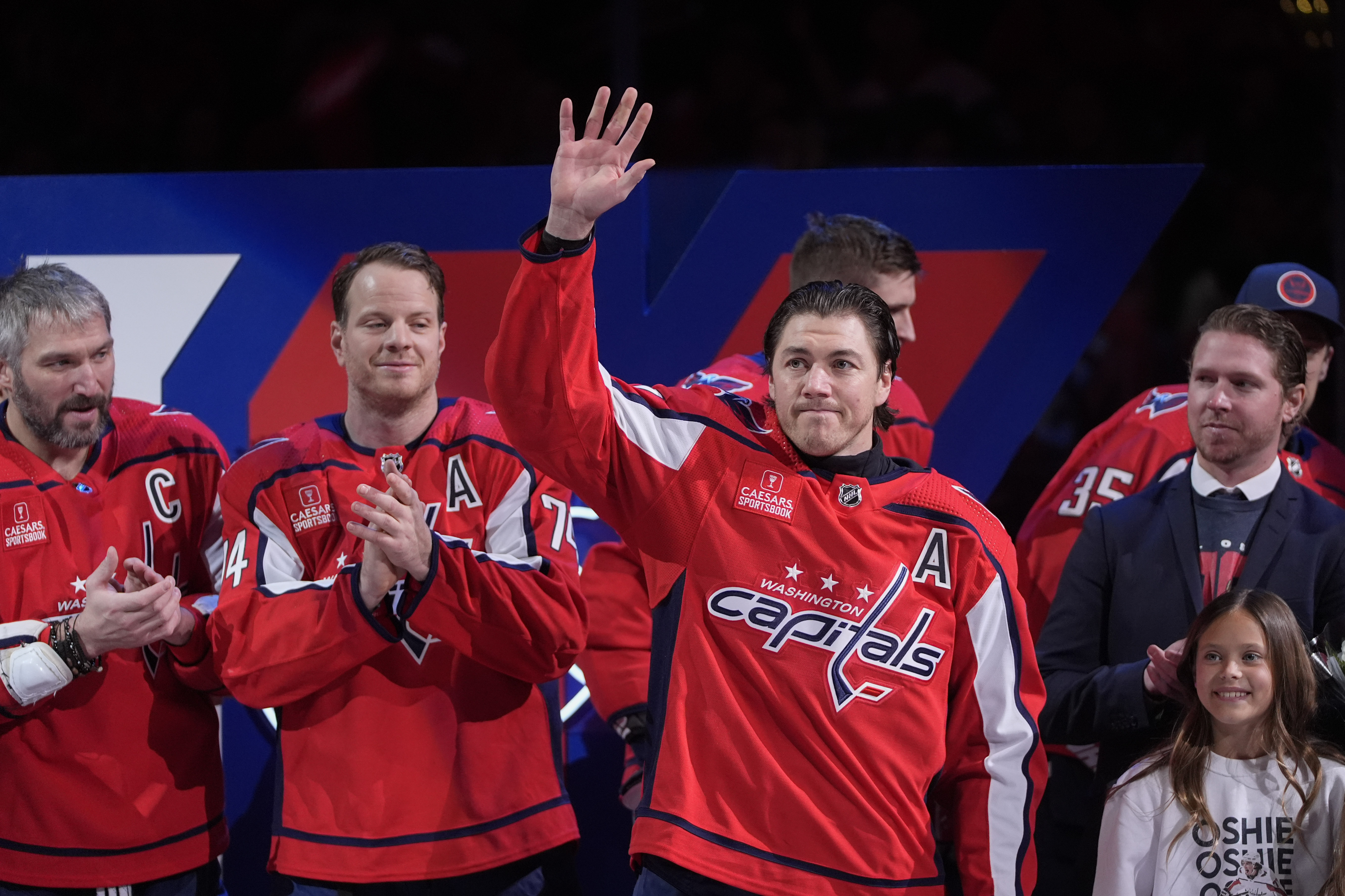 FILE - Washington Capitals right wing T.J. Oshie waves as he acknowledges the crowd as teammates, from left to right, left wing Alex Ovechkin, defenseman John Carlson and center Nicklas Backstrom applaud during a ceremony to mark Oshie's playing in 1000 career NHL games before an NHL hockey game against the Winnipeg Jets, March 24, 2024, in Washington.