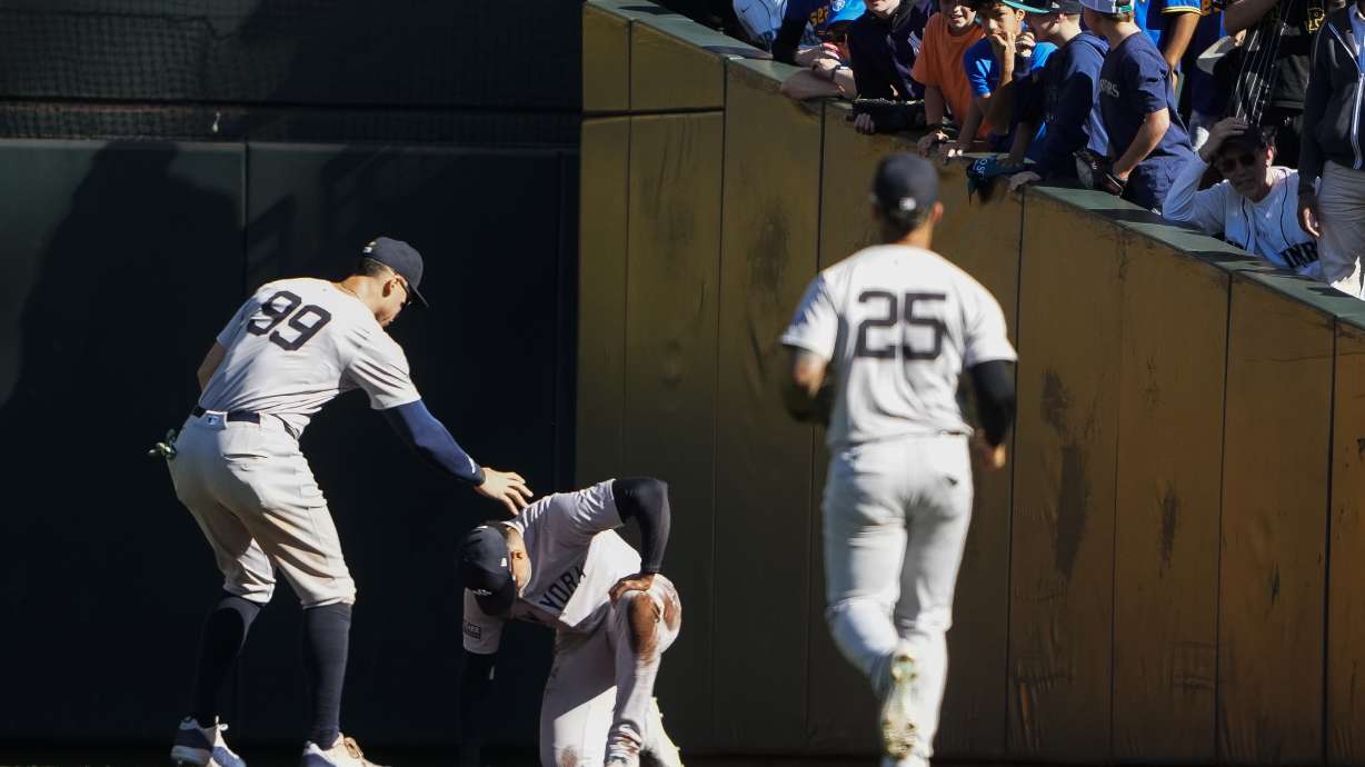 New York Yankees right fielder Juan Soto, center, is checked on by center fielder Aaron Judge (99) and second baseman Gleyber Torres (25) after colliding with the wall after making a catch on a foul ball from Seattle Mariners' Jorge Polanco during the seventh inning of a baseball game Thursday, Sept. 19, 2024, in Seattle.