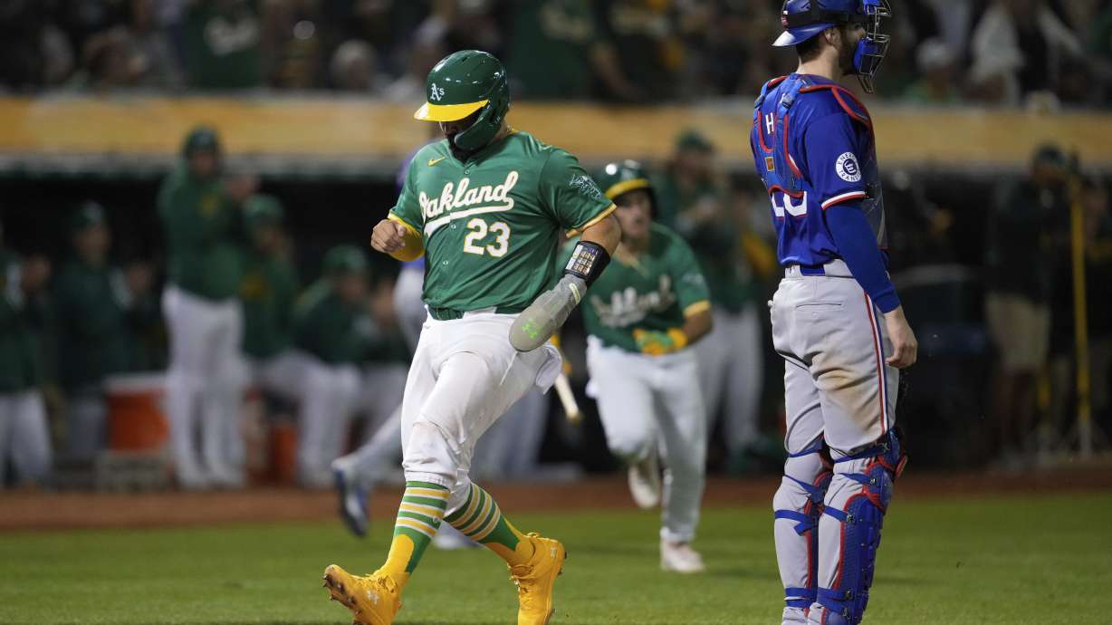 Oakland Athletics' Shea Langeliers (23) scores next to Texas Rangers catcher Jonah Heim on Zack Gelof's sacrifice fly during the sixth inning of a baseball game Tuesday, Sept. 24, 2024, in Oakland, Calif.