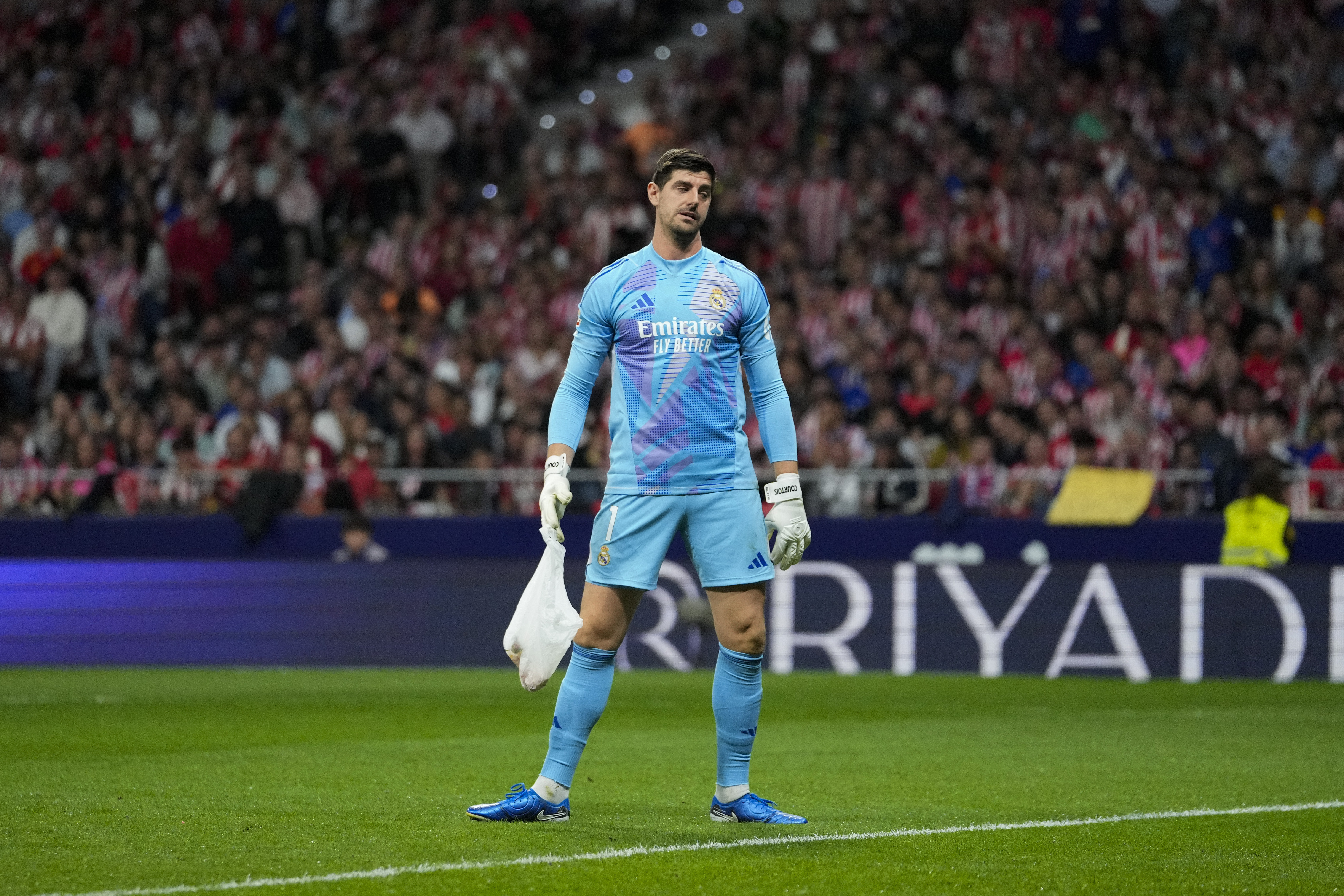 Real Madrid's goalkeeper Thibaut Courtois holds a bag, thrown by Atletico Madrid fans, during the La Liga soccer match between Atletico Madrid and Real Madrid at the Metropolitano stadium in Madrid, Spain, Sunday, Sept. 29, 2024.