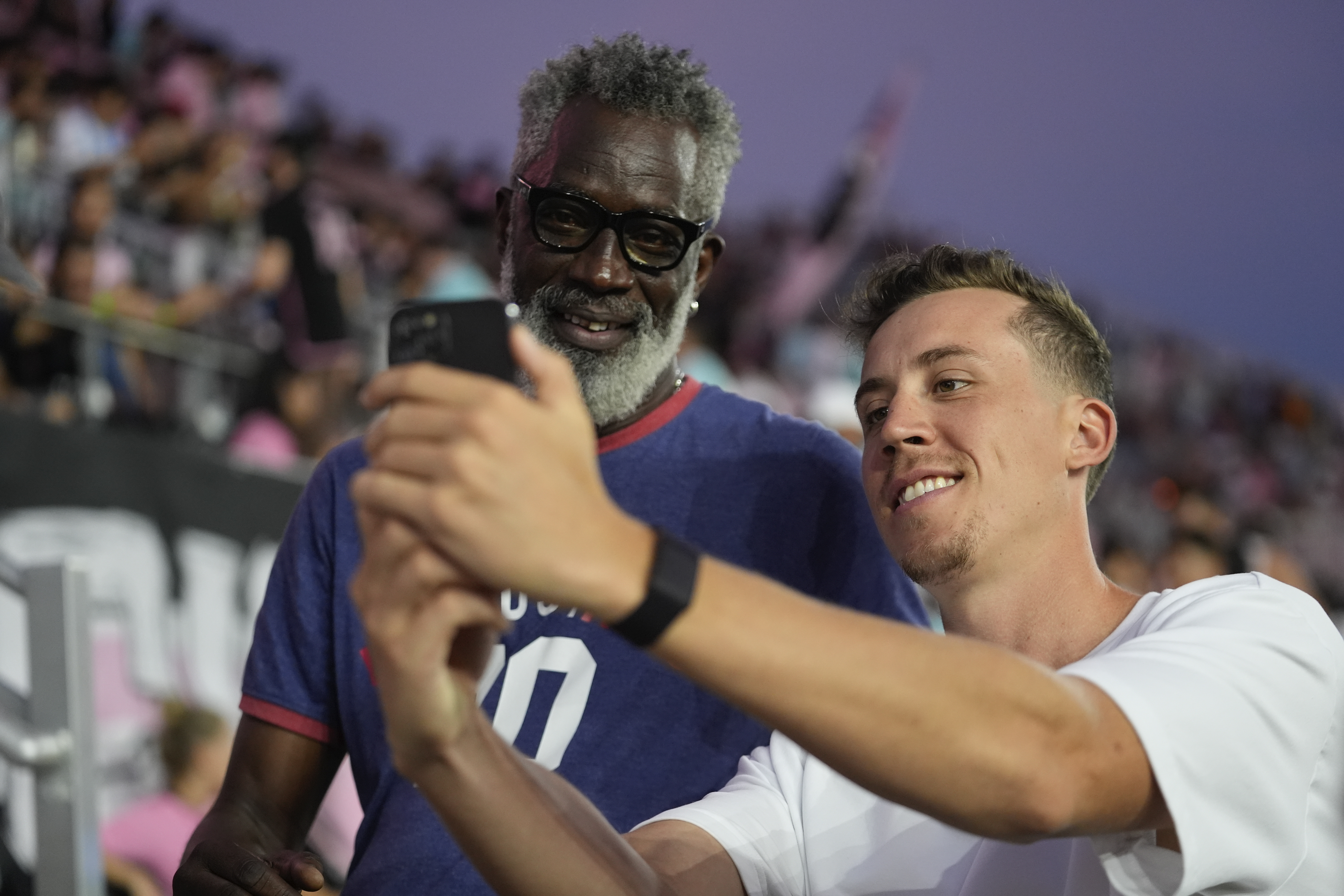 Miami Heat forward Duncan Robinson, right, takes a selfie for a fan in the stands, as he stands on the sideline before the start of an MLS soccer match between Inter Miami and Charlotte FC, Saturday, Sept. 28, 2024, in Fort Lauderdale, Fla. 
