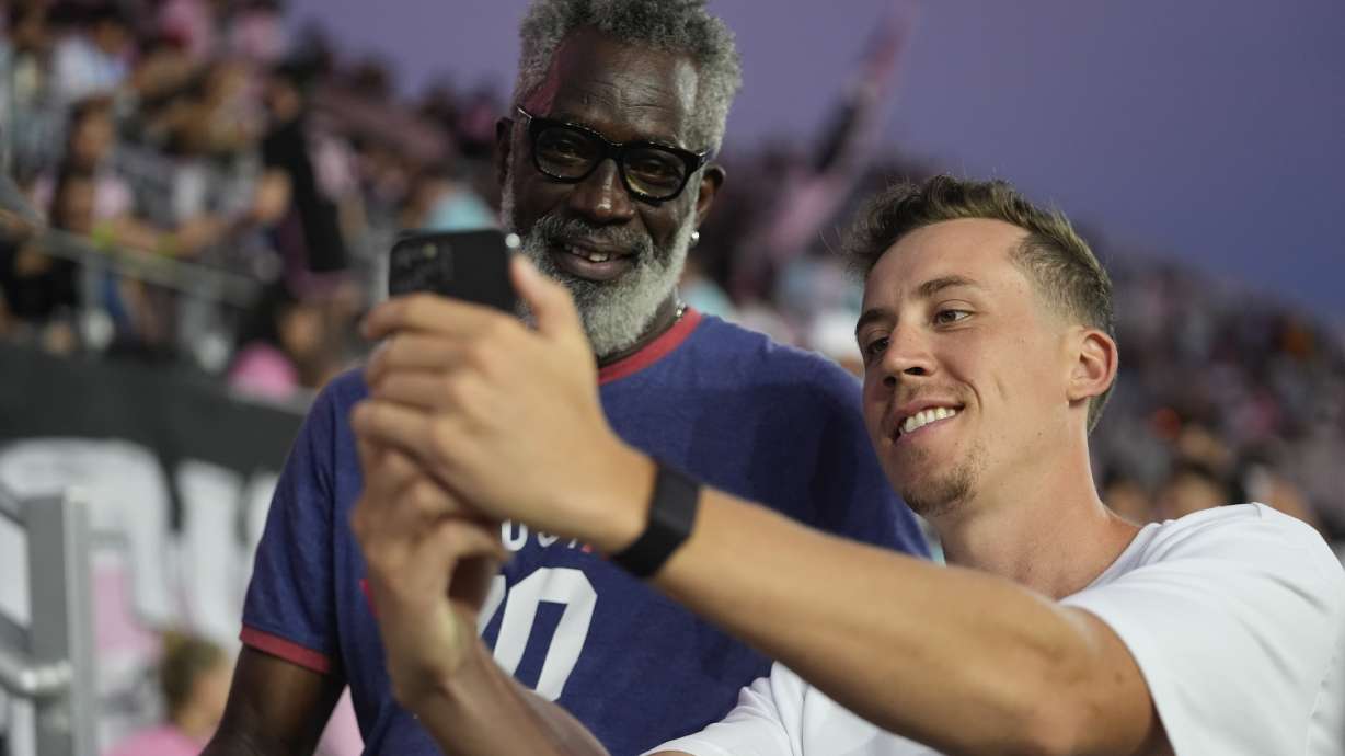 Miami Heat forward Duncan Robinson, right, takes a selfie for a fan in the stands, as he stands on the sideline before the start of an MLS soccer match between Inter Miami and Charlotte FC, Saturday, Sept. 28, 2024, in Fort Lauderdale, Fla.