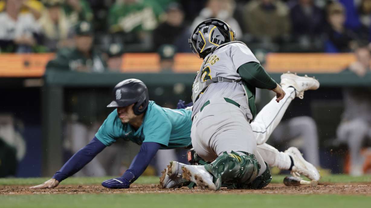 Seattle Mariners' Leo Rivas scores as Oakland Athletics catcher Shea Langeliers reaches to tag during the tenth inning in a baseball game, Saturday, Sept. 28, 2024, in Seattle. The Mariners won 7-6.
