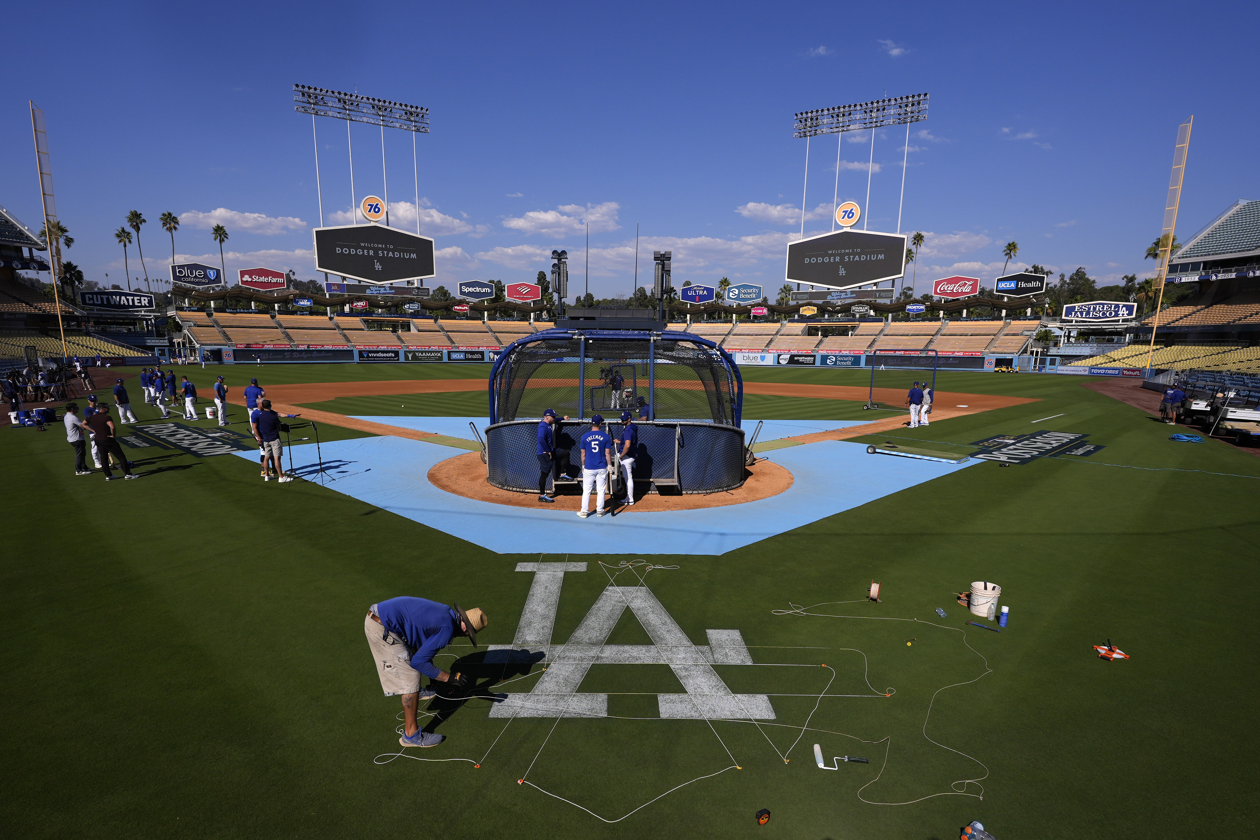 A Los Angeles Dodgers grounds crew member paints a logo on the field prior to practice in preparation for Game 1 of a baseball NL Division Series against the San Diego Padres, Thursday, Oct. 3, 2024, in Los Angeles.