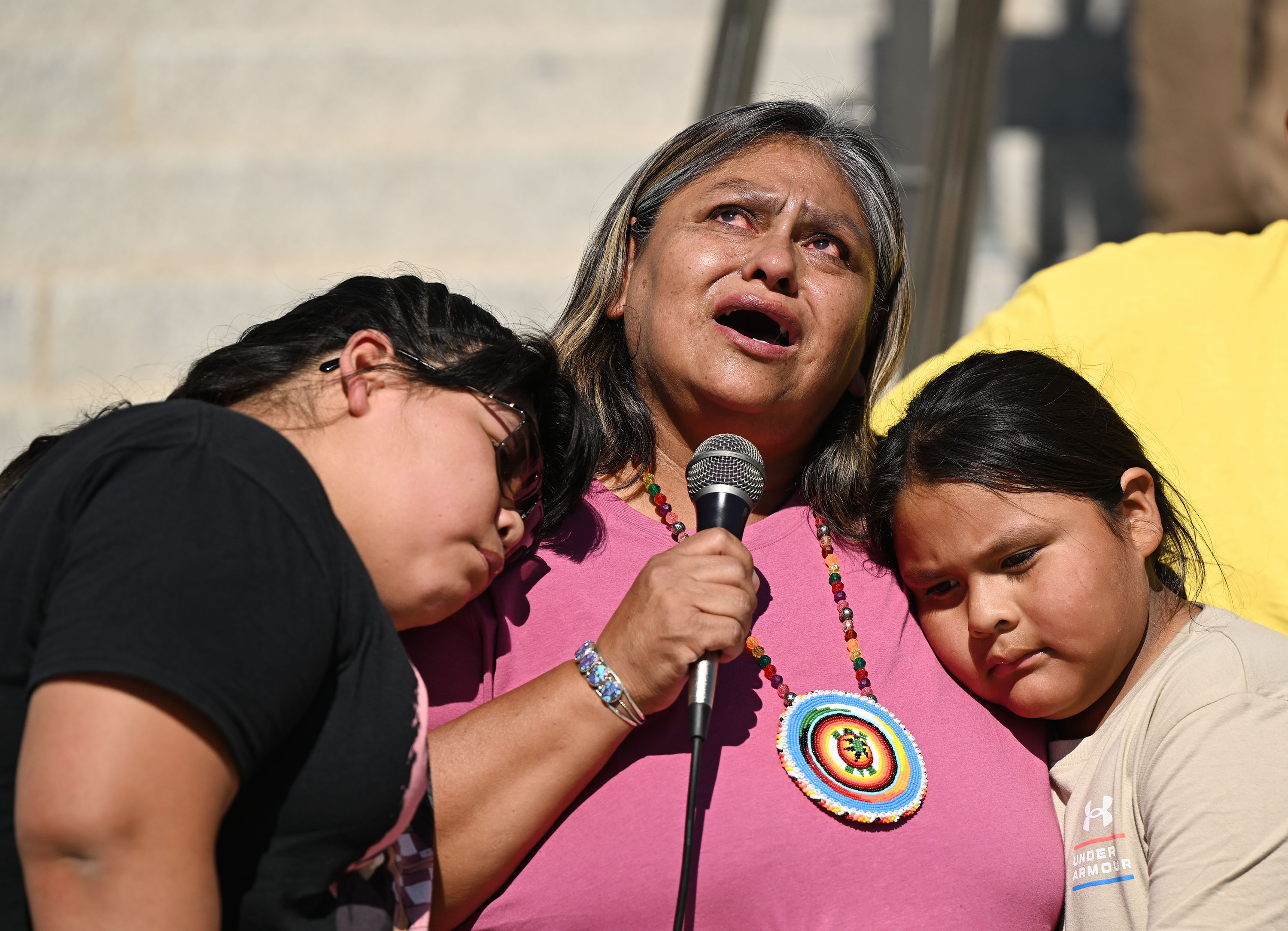 Yolanda Badback, of the White Mesa Concerned Community Protect, looks up toward the heavens as she talks about her brother who passed away, as her grandchildren Amari Badback and Juniper Thomas hug her, and she speaks at a rally against bringing uranium to their homelands, at the Capitol on Friday.