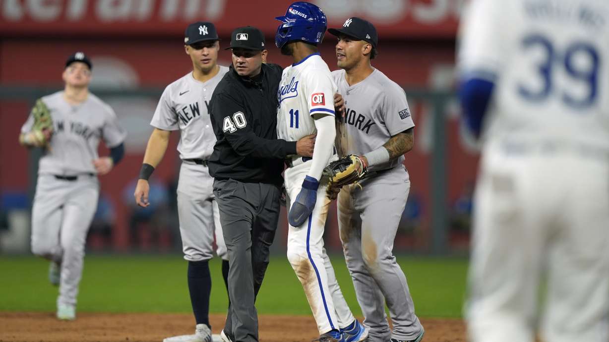 Umpire Roberto Ortiz holds back Kansas City Royals' Maikel Garcia (11) after being tagged out by New York Yankees shortstop Anthony Volpe as the benches empty after a double play during the sixth inning in Game 4 of an American League Division baseball playoff series Thursday, Oct. 10, 2024, in Kansas City, Mo.