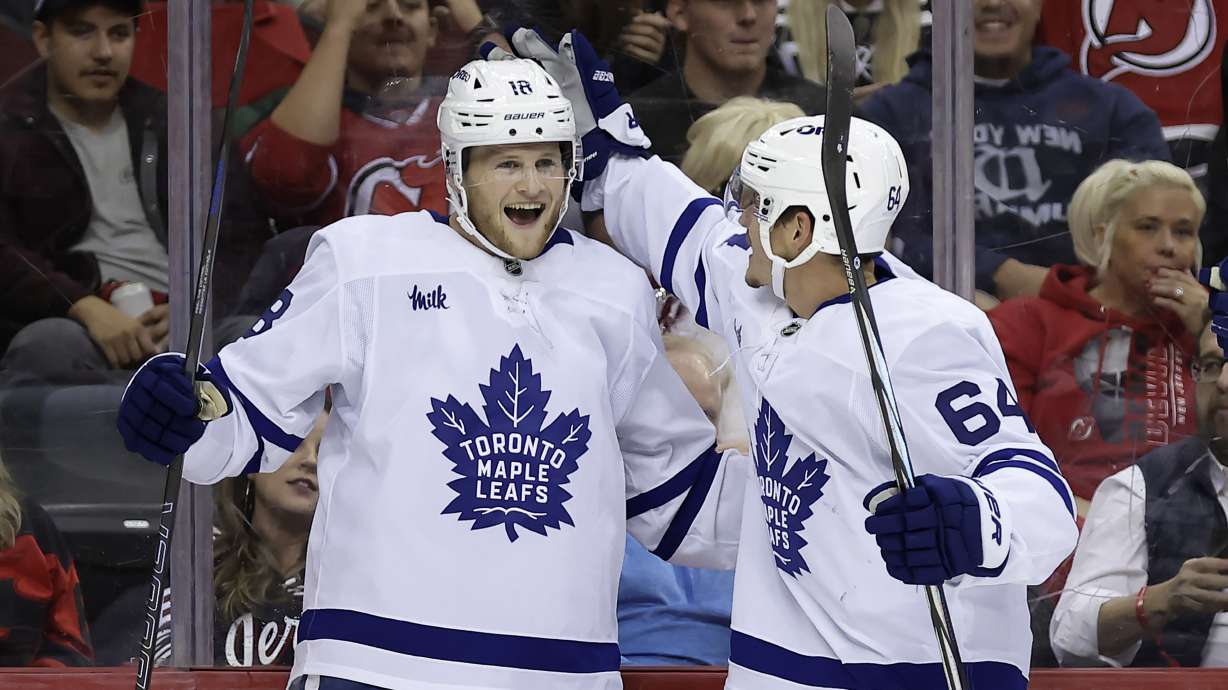Toronto Maple Leafs center Steven Lorentz (18) is congratulated by David Kampf (64) after scoring during the first period of an NHL hockey game against the New Jersey Devils, Thursday, Oct. 10, 2024, in Newark, N.J.