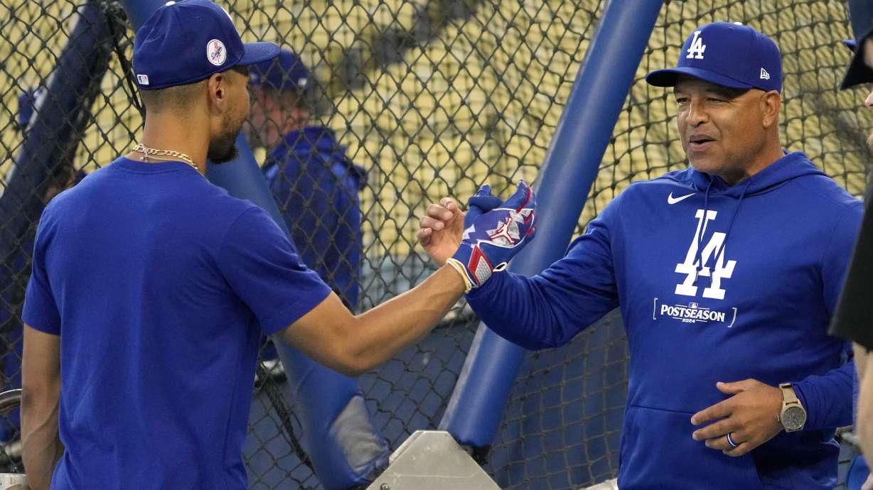 Los Angeles Dodgers' Mookie Betts, left, and manager Dave Roberts greet each other during practice in preparation for Game 1 of a baseball NL Championship Series against the New York Mets, Saturday, Oct. 12, 2024, in Los Angeles.