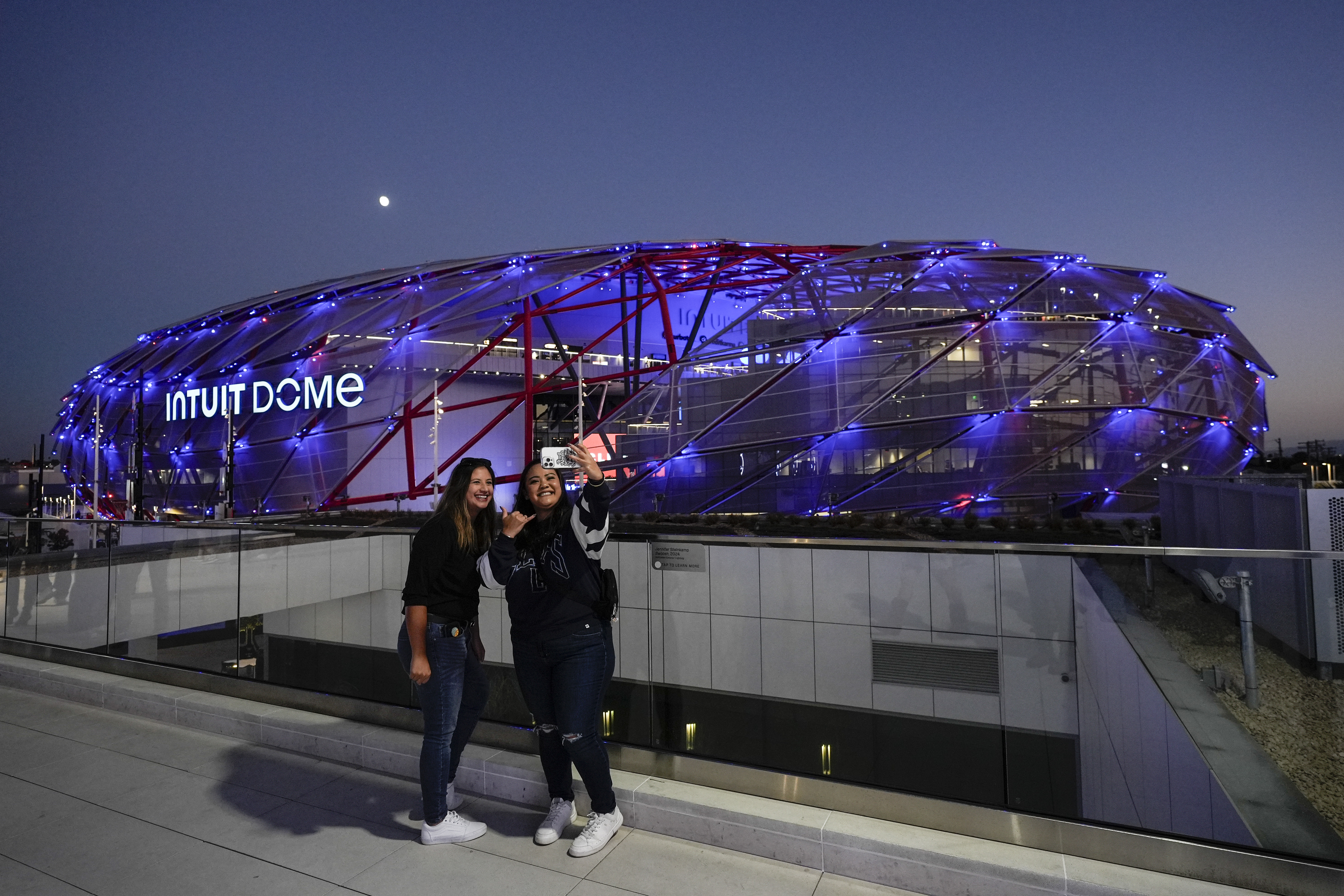 Two fans take a selfie outside the Intuit Dome, the new home of the Los Angeles Clippers, before the team's NBA preseason basketball game against the Dallas Mavericks Monday, Oct. 14, 2024, in Inglewood, Calif.