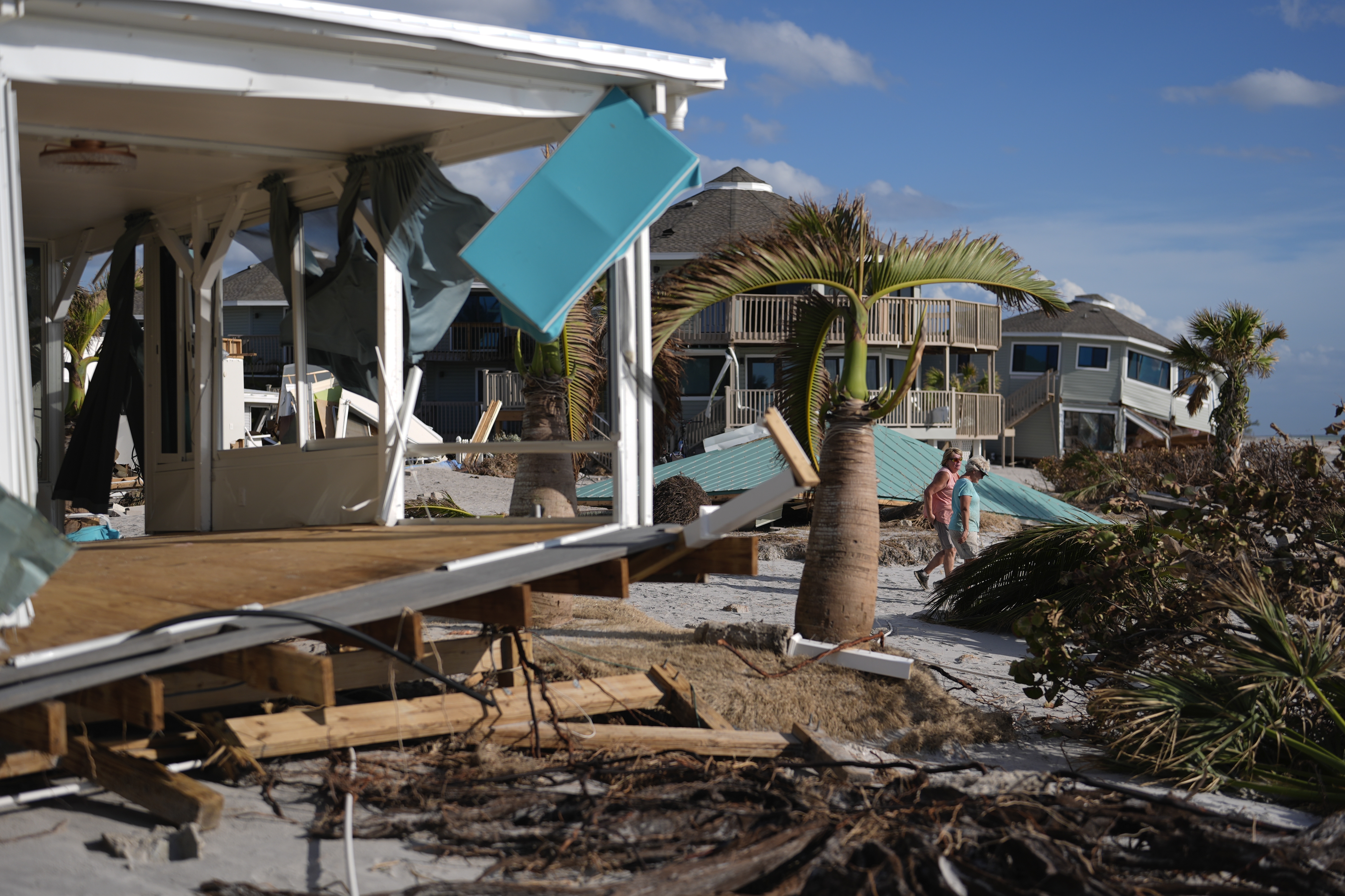 Resident Kerry Flynn, right, and a friend walk past a damaged home and the displaced roof of their 55+ mobile home community's tiki hut after the passage of Hurricane Milton, on Manasota Key, in Englewood, Fla., Sunday. The hurricanes Milton and Helene are proving to have caused billions in damage.