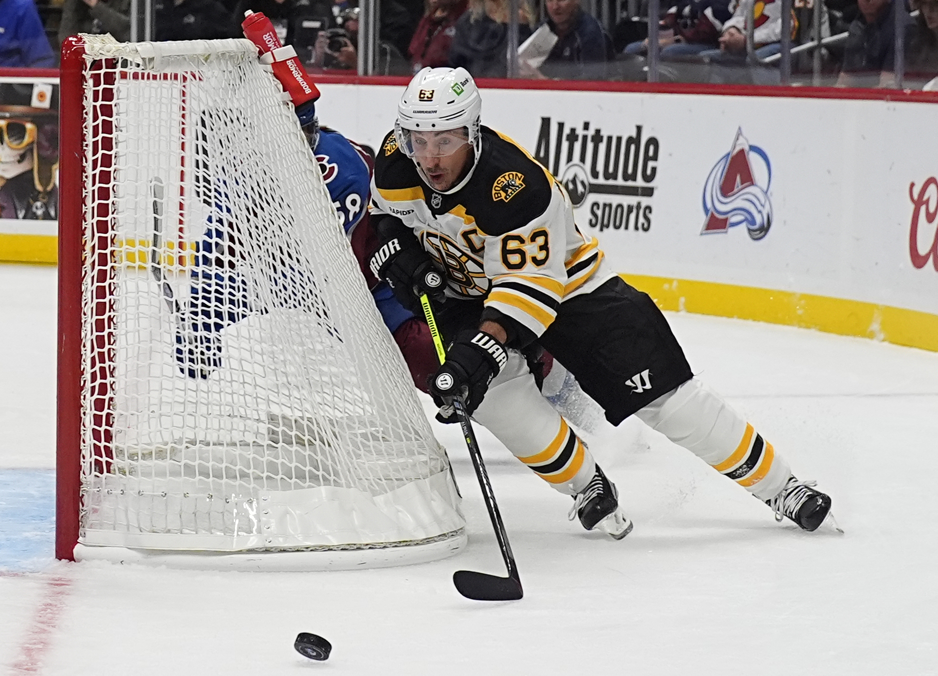 Boston Bruins left wing Brad Marchand, front, wraps around the net with the puck as Colorado Avalanche defenseman Oliver Kylington pursues in the second period of an NHL hockey game Wednesay, Oct. 16, 2024, in Denver.