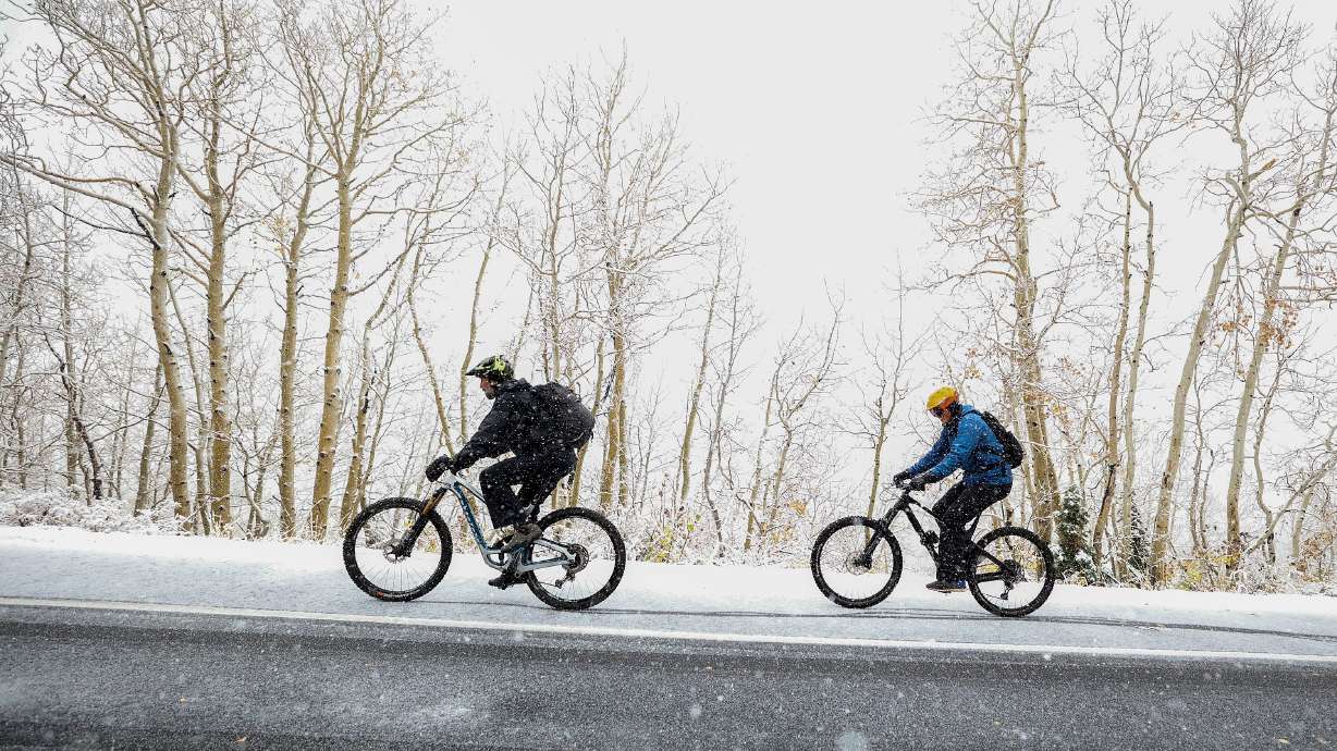 Stefan Vest and Leo MacCormack bike up Guardsman Pass during a snow storm on Thursday. The wintry storm has been helpful for crews battling wildfires and setting up resorts for the upcoming ski season.