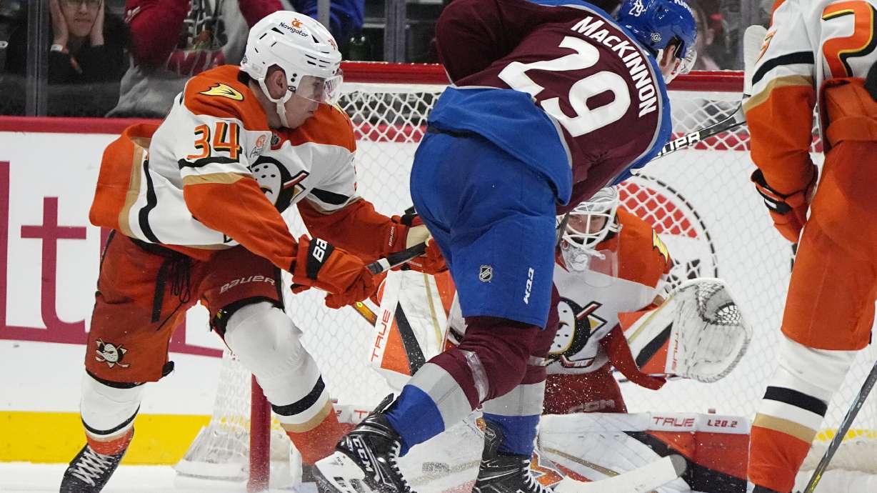 Colorado Avalanche center Nathan MacKinnon (29) shoots the puck for the winning goal as Anaheim Ducks goaltender Lukas Dostal, back right, and defenseman Pavel Mintyukov, left, cover in overtime of an NHL hockey game Friday, Oct. 18, 2024, in Denver.