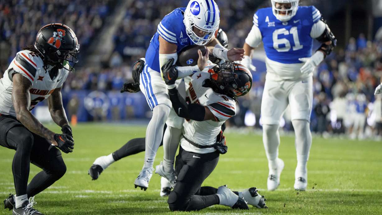 BYU quarterback Jake Retzlaff, center top, runs the ball for a touchdown past a tackle-attempt by Oklahoma State safety Lyrik Rawls, center bottom, in the first half of an NCAA college football game, Friday, Oct. 18, 2024, in Provo, Utah.