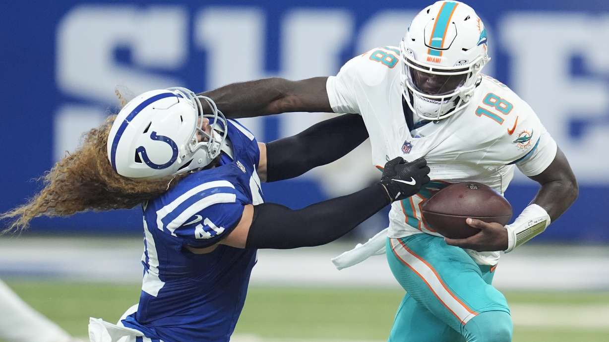 Miami Dolphins quarterback Tyler Huntley (18) blocks a tackle by Indianapolis Colts linebacker Grant Stuard (41) as he runs the ball during the first half of an NFL football game, Sunday, Oct. 20, 2024 in Indianapolis.