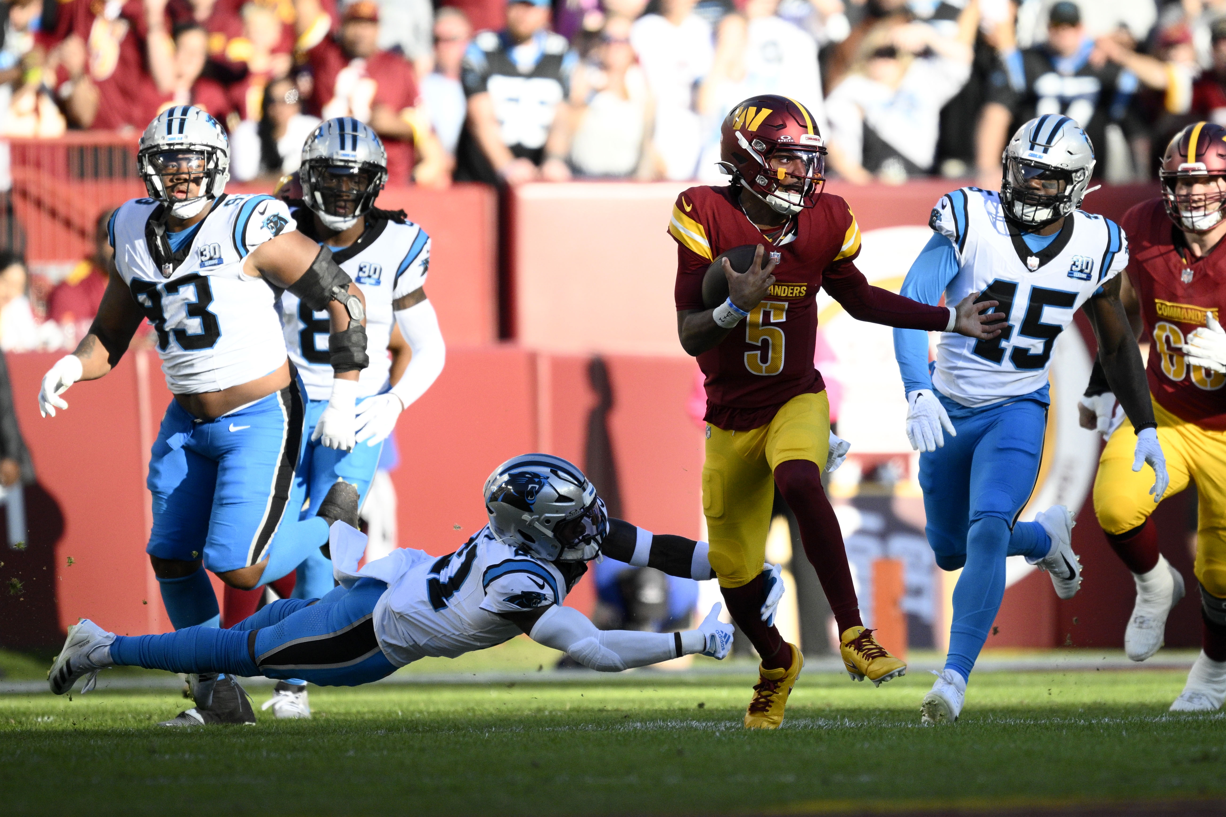 Washington Commanders quarterback Jayden Daniels (5) runs from Carolina Panthers safety Nick Scott (21) and linebacker Marquis Haynes Sr. (45) during the first half of an NFL football game, Sunday, Oct. 20, 2024, in Landover, Md.