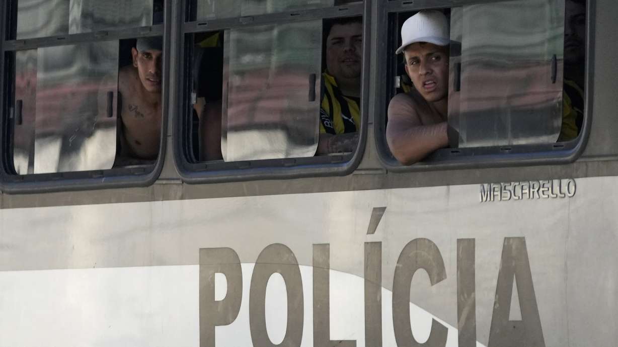 Fans of Uruguay’s Penarol soccer team peer from inside a police bus as they arrive at a police station after being detained for fighting with police on the beach in Rio de Janeiro, Brazil, Wednesday, Oct. 23, 2024. Penarol fans are in Rio for a semi-final Copa Libertadores game against Brazil's Botafogo.