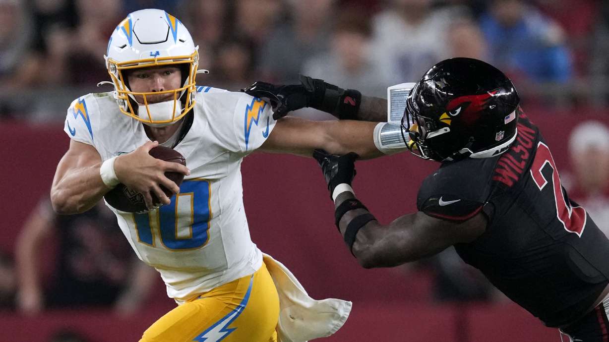 Los Angeles Chargers quarterback Justin Herbert (10) runs from Arizona Cardinals linebacker Mack Wilson Sr. (2) during the second half of an NFL football game, Monday, Oct. 21, 2024, in Glendale Ariz.