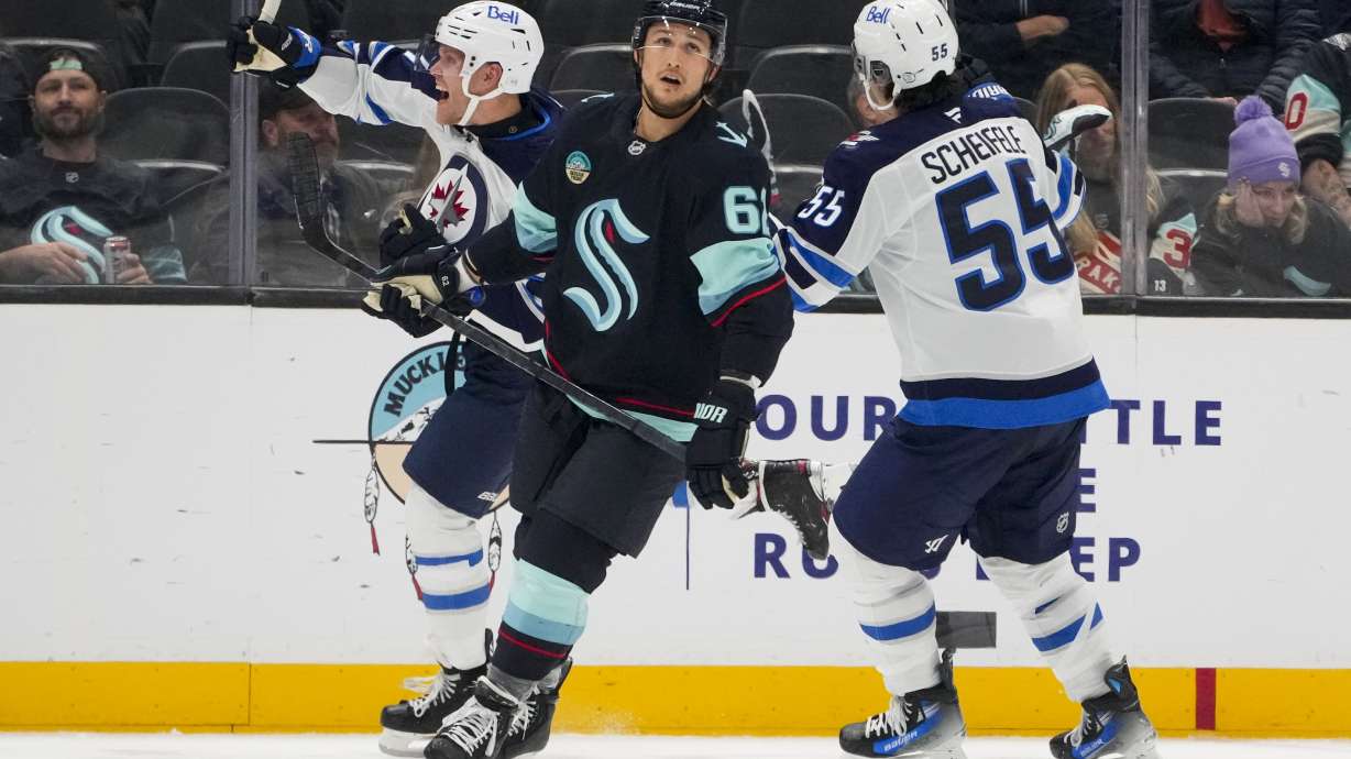 Winnipeg Jets left wing Nikolaj Ehlers, left, celebrates his game-winning goal with center Mark Scheifele (55) as Seattle Kraken defenseman Brandon Montour, center, looks away during overtime of an NHL hockey game Thursday, Oct. 24, 2024, in Seattle. The Jets won 4-3 in overtime.