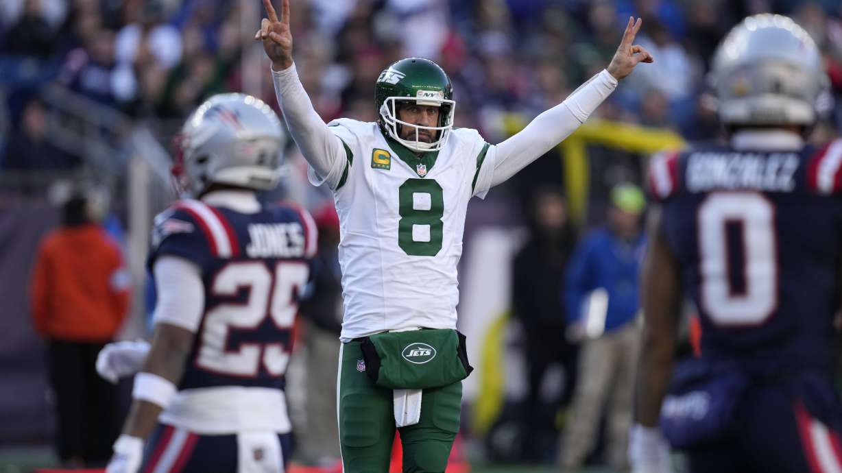 New York Jets quarterback Aaron Rodgers (8) celebrates in front of New England Patriots cornerback Marcus Jones (25) and cornerback Christian Gonzalez (0) after Jets running back Braelon Allen ran for a touchdown in the second half of an NFL football game, Sunday, Oct. 27, 2024, in Foxborough, Mass.