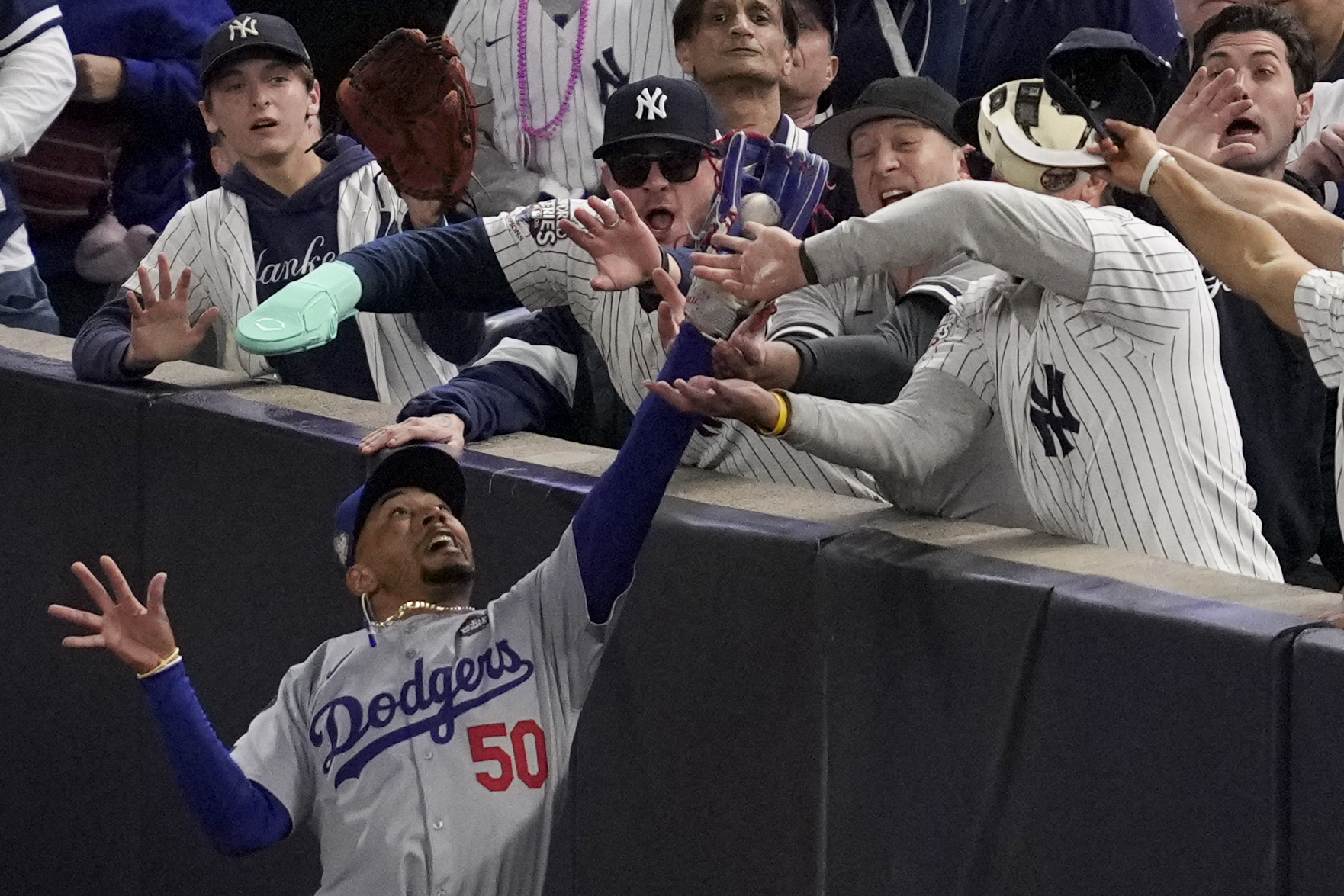 Fans interfere with a foul ball caught by Los Angeles Dodgers right fielder Mookie Betts during the first inning in Game 4 of the baseball World Series against the New York Yankees, Tuesday, Oct. 29, 2024, in New York. 