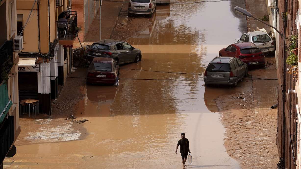 A man carrying water walks through flooded streets in Valencia, Spain, Wednesday, Oct. 30, 2024.