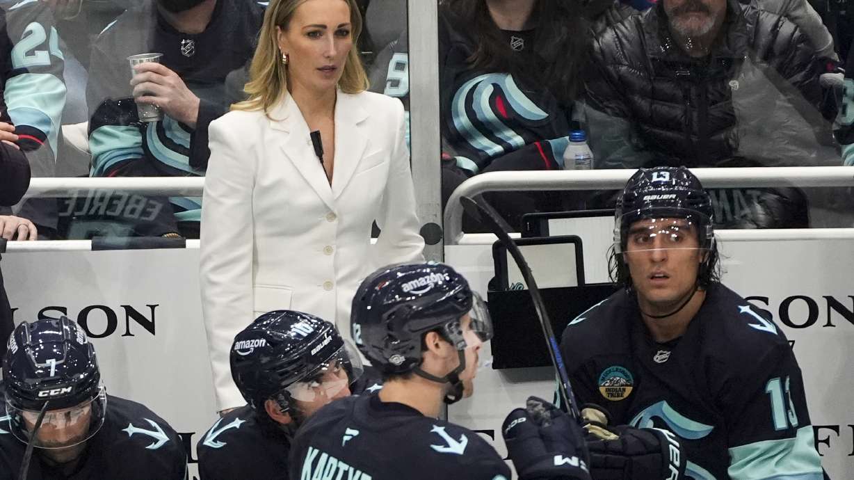 FILE - Seattle Kraken assistant coach Jessica Campbell, rear, looks on from the bench during the first period of an NHL hockey game against the St. Louis Blues, Tuesday, Oct. 8, 2024, in Seattle.