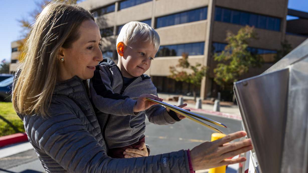 Katherine Kitterman holds her 2-year-old son, Ethan Roberts, as he puts her ballot in a drop box at the Salt Lake County Government Center in Salt Lake City on Monday. Kitterman brought her son so he could see her voting and follow her example.