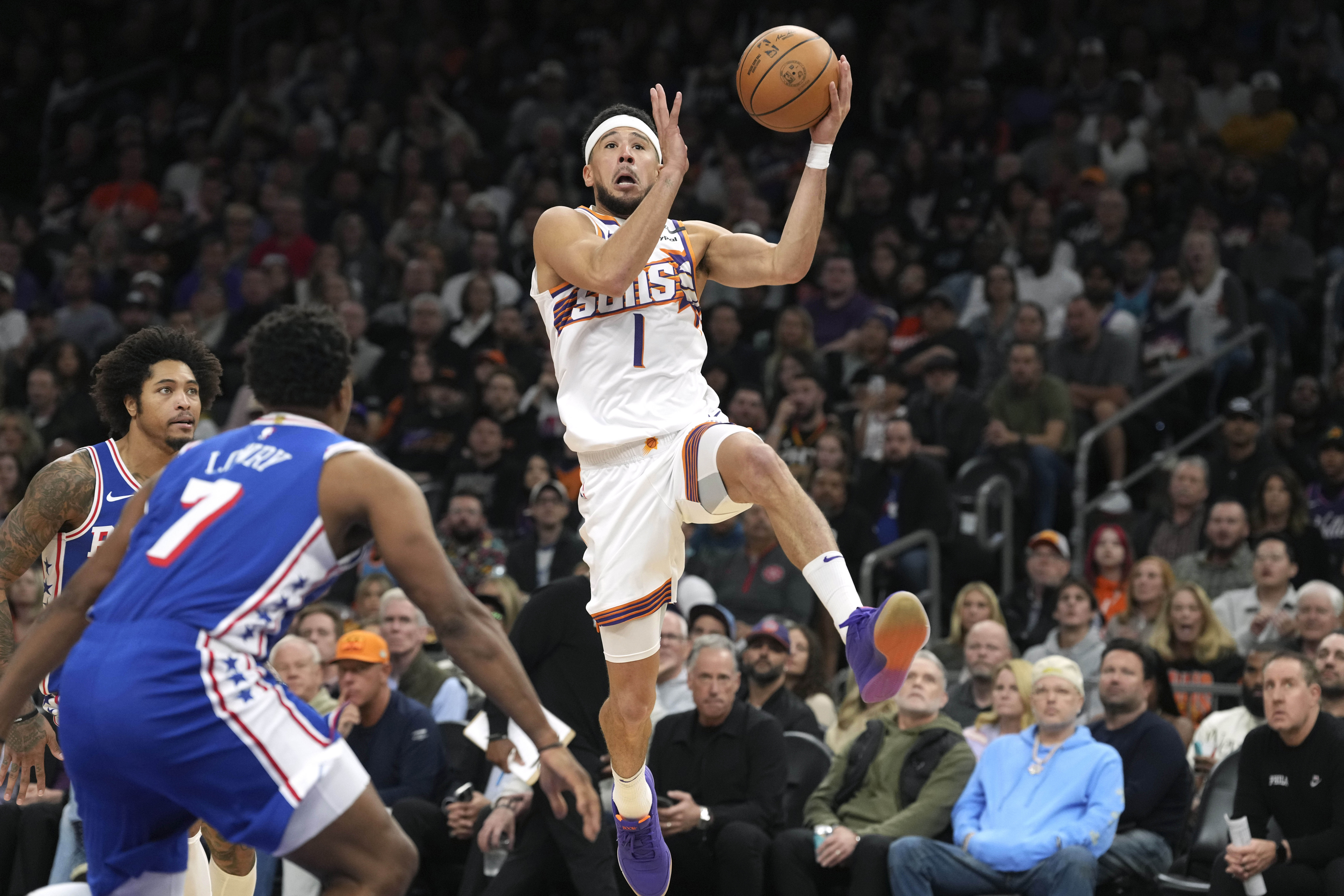Phoenix Suns guard Devin Booker (1) drives past Philadelphia 76ers guard Kyle Lowry (7) and 76ers guard Kelly Oubre Jr. during the second half of an NBA basketball game Monday, Nov. 4, 2024, in Phoenix.