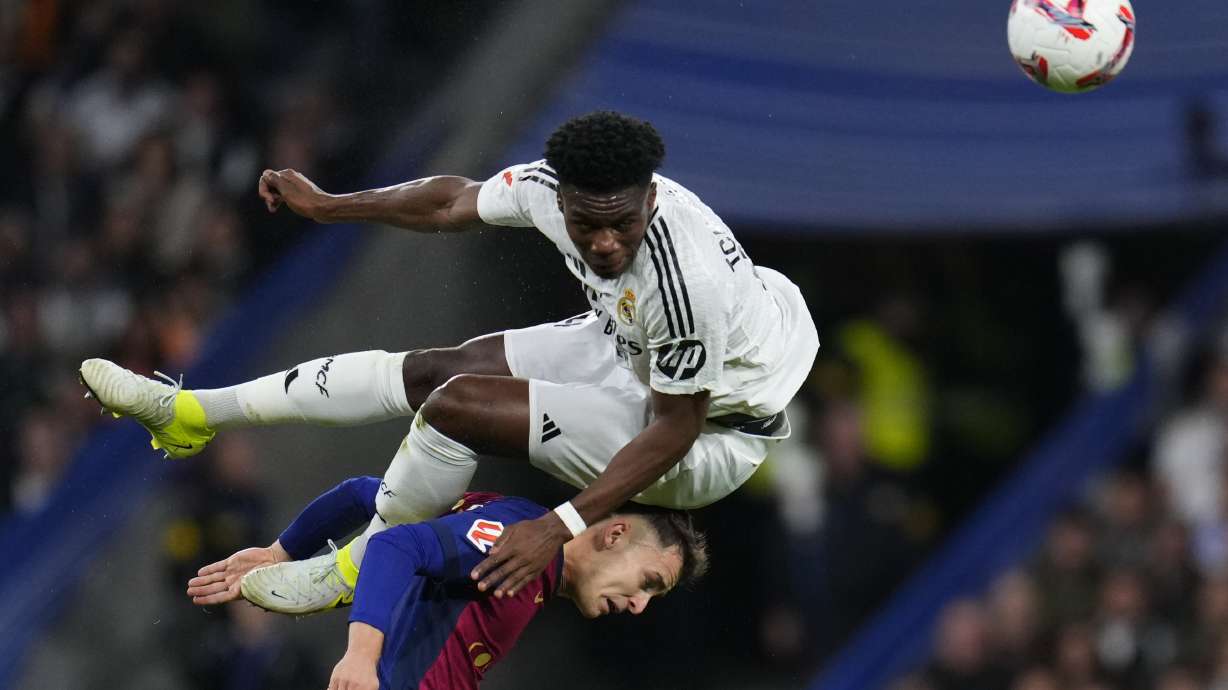 Real Madrid's Aurelien Tchouameni jumps for a header on top of Barcelona's Marc Casado during a Spanish La Liga soccer match between Real Madrid and Barcelona at the Santiago Bernabeu stadium in Madrid, Spain, Saturday, Oct. 26, 2024.