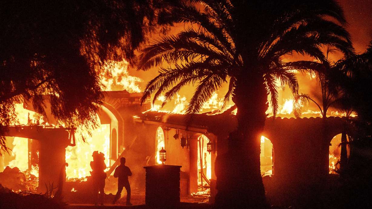 Television reporters film as flames from the Mountain Fire consume a home in Camarillo, Calif., on Wednesday.