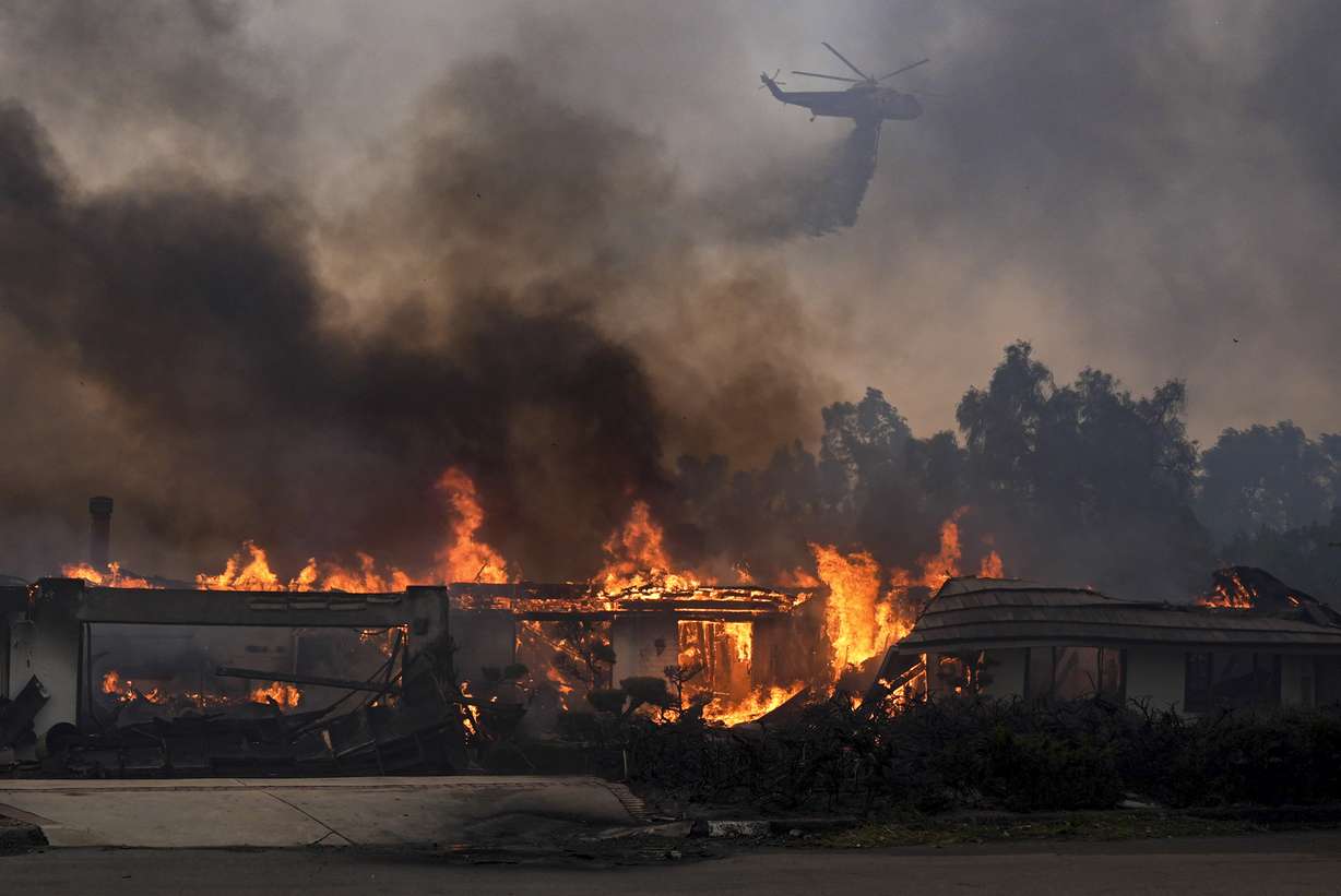 A helicopter drops water over a burning home in the Mountain fire, Wednesday, near Camarillo, Calif.