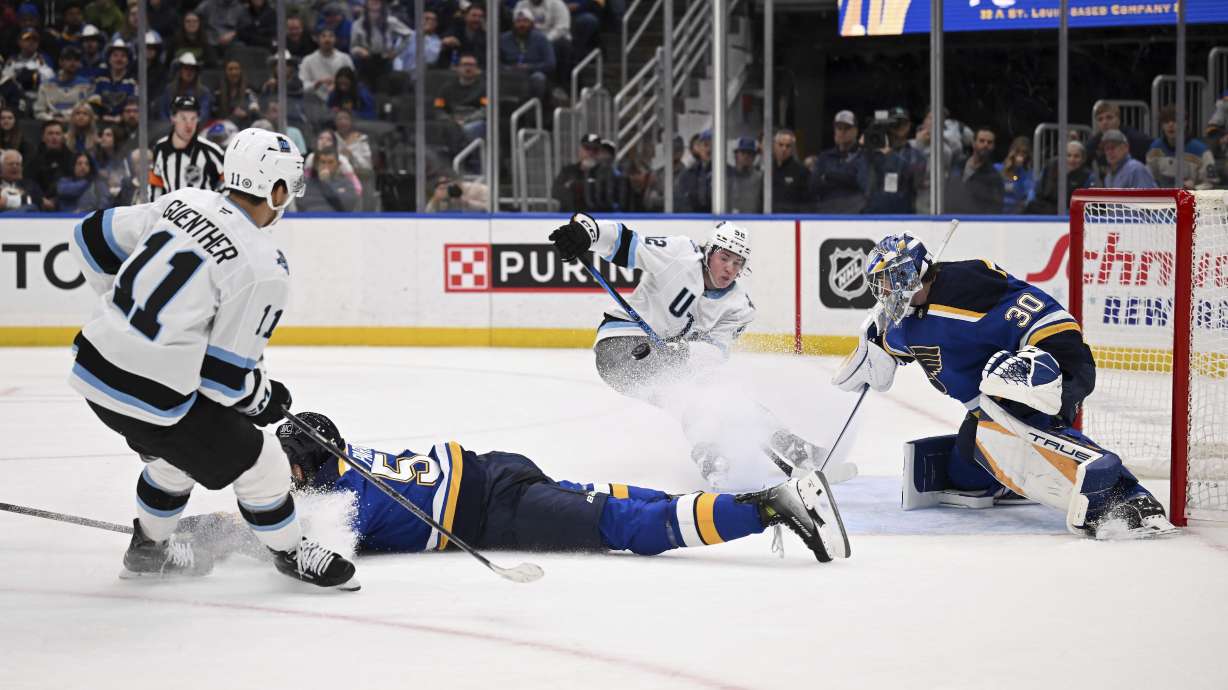 Utah Hockey Club's Dylan Guenther (11) and Utah Hockey Club's Vladislav Kolyachonok (52), back center, watch on as St. Louis Blues' Joel Hofer (30) and St. Louis Blues' Colton Parayko (55) defend the net during the third period of an NHL hockey game Thursday, Nov. 7, 2024, in St. Louis.