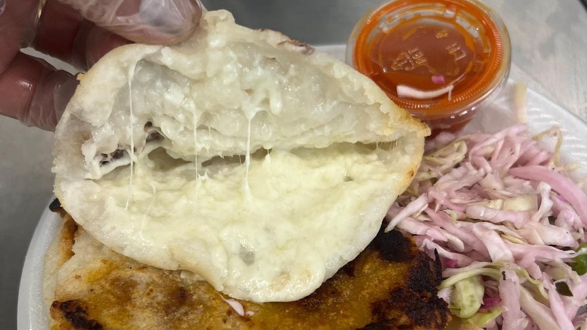 The undated photo shows an open pupusa with curtido and sauce on the side.