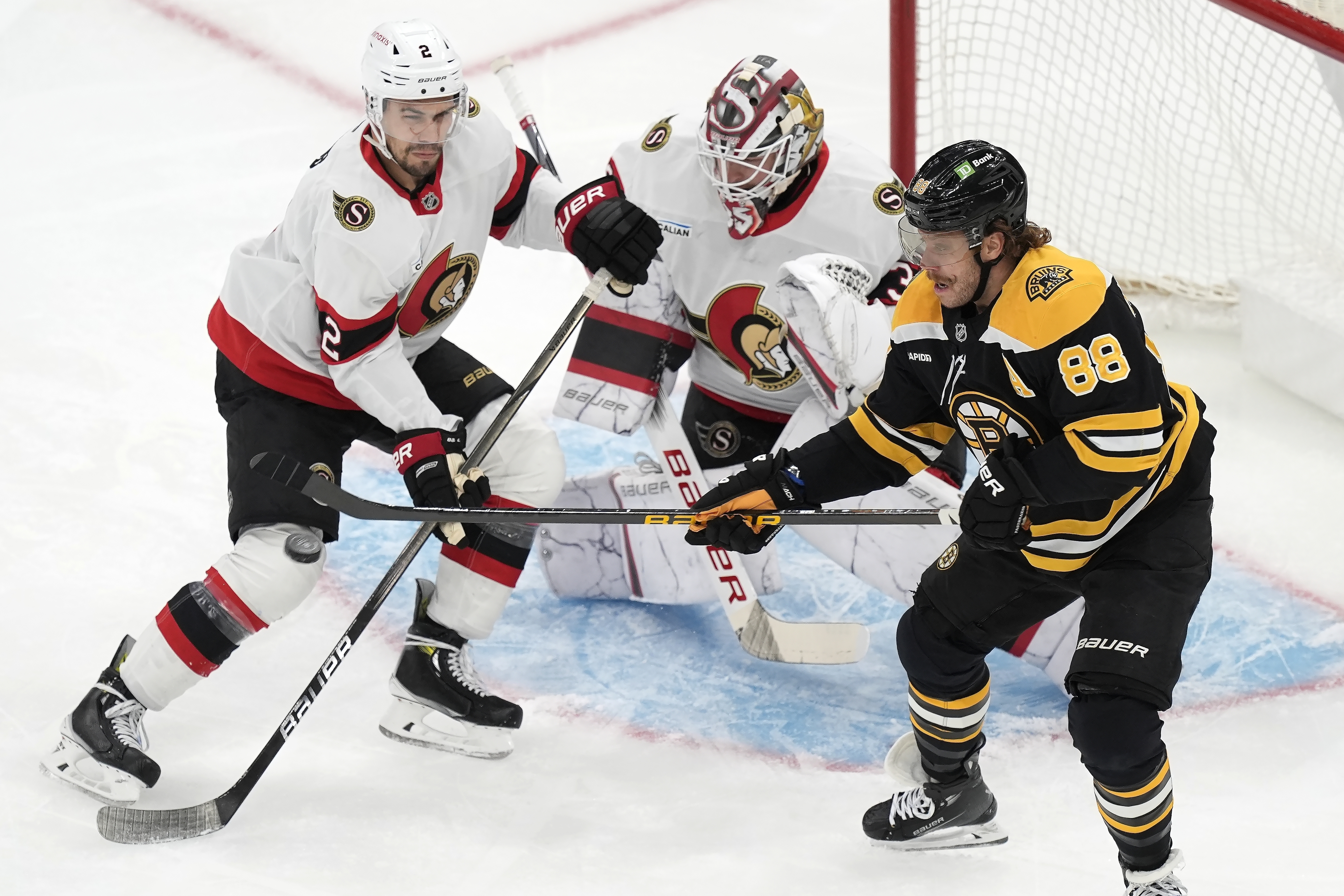 Boston Bruins' David Pastrnak (88) tries to control the puck against Ottawa Senators' Artem Zub (2) and Linus Ullmark (35) during the first period of an NHL hockey game, Saturday, Nov. 9, 2024, in Boston.