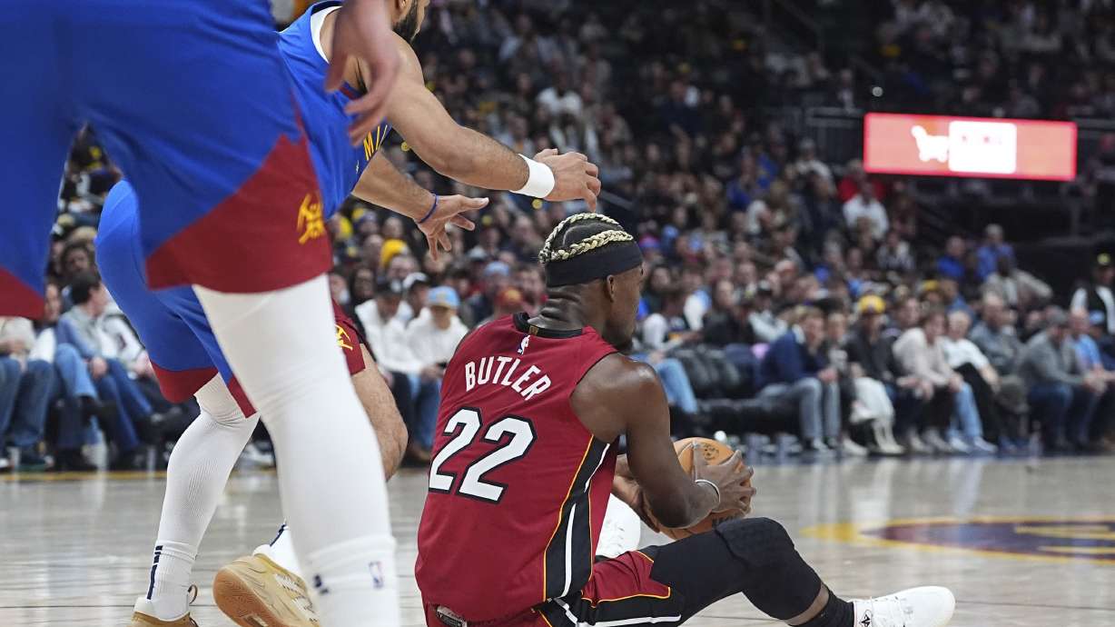 Miami Heat forward Jimmy Butler, right, looks to pass the ball after falling on the floor as Denver Nuggets guard Jamal Murray defends in the first half of an NBA basketball game Friday, Nov. 8, 2024, in Denver.