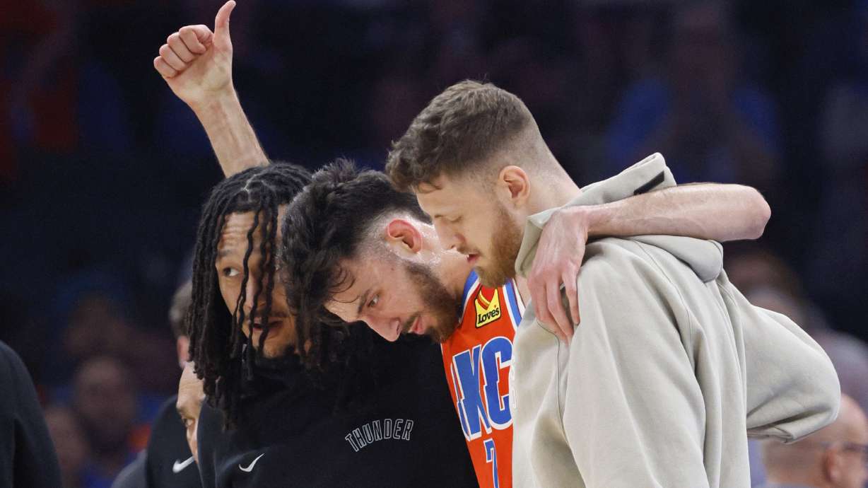 Oklahoma City Thunder forward Chet Holmgren, center, gives a thumbs-up as he is helped off the court by Thunder forward Jaylin Williams, left, and center Isaiah Hartenstein, right, during the first half of an NBA basketball game against the Golden State Warriors, Sunday, Nov. 10, 2024, in Oklahoma City.