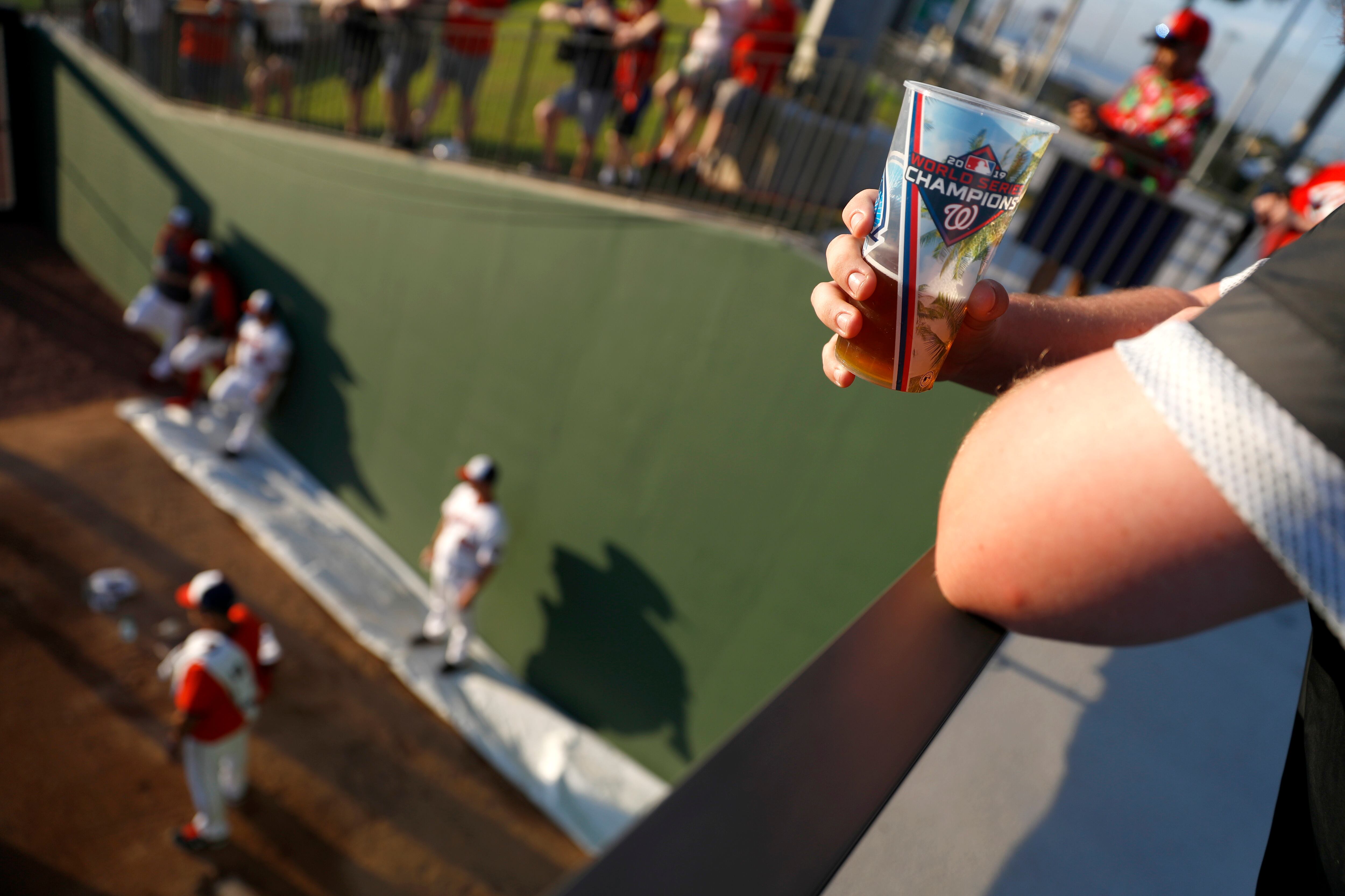 A spectator drinks from a souvenir cup as he watches pitchers warm up before a spring training baseball game against the St. Louis Cardinals, March 5, 2020, in West Palm Beach, Fla.