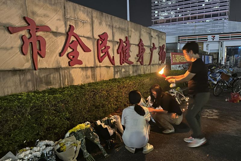 A woman lights a candle as offering near flowers placed outside the "Zhuhai People's Fitness Plaza" where police say a man rammed his car into people exercising at the sports center, killing some and injuring others in Zhuhai, China on Tuesday.