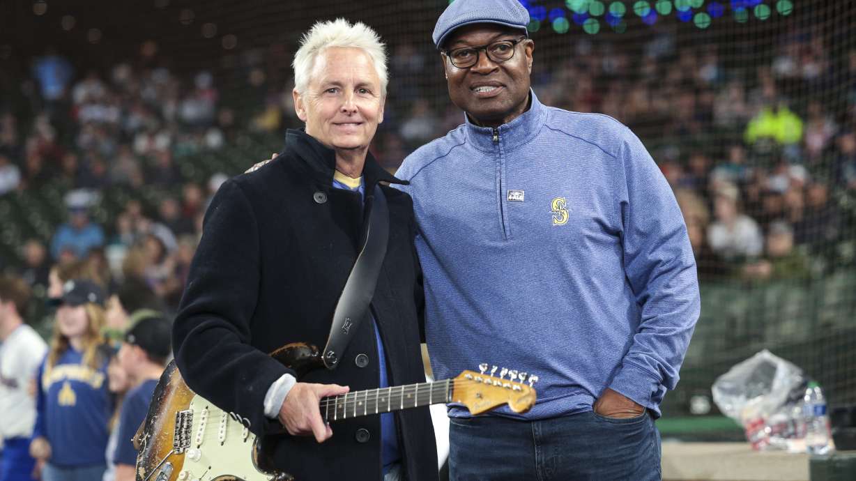 Pearl Jam guitarist Mike McCready, left, and Mariners broadcaster Dave Sims pose for a photo before McCready performs the national anthem at a baseball game between the Seattle Mariners and the Los Angeles Angels, Sunday, June 2, 2024, in Seattle. Sims is now going to be a play-by-play announcer for the New York Yankees.