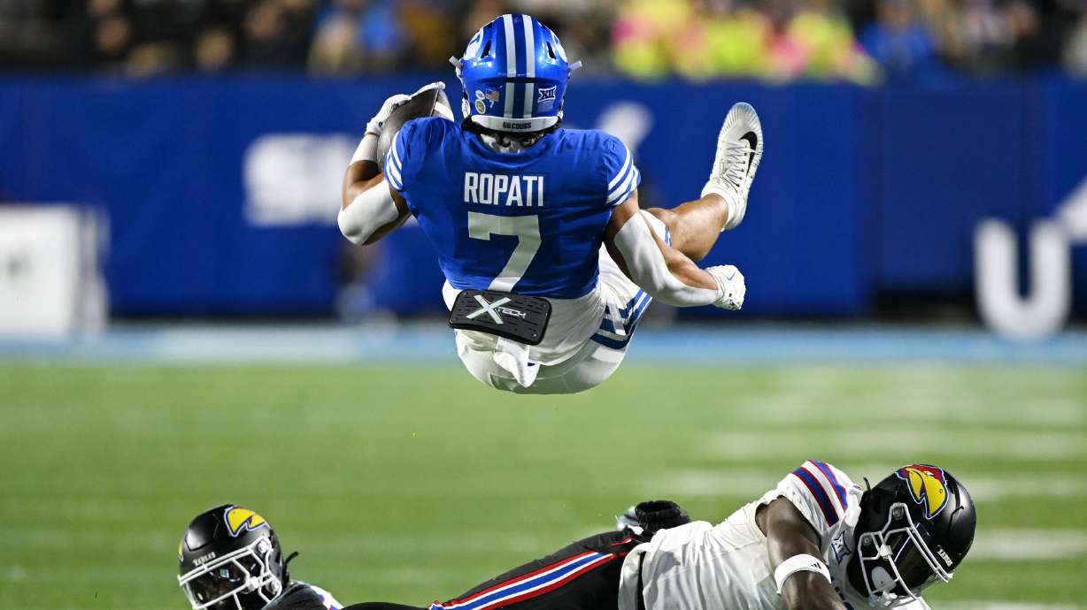 Brigham Young running back Hinckley Ropati (7) is flipped around after being hit by Kansas linebacker JB Brown (1) as BYU and Kansas play at LaVell Edwards Stadium in Provo on Saturday, Nov. 16, 2024.