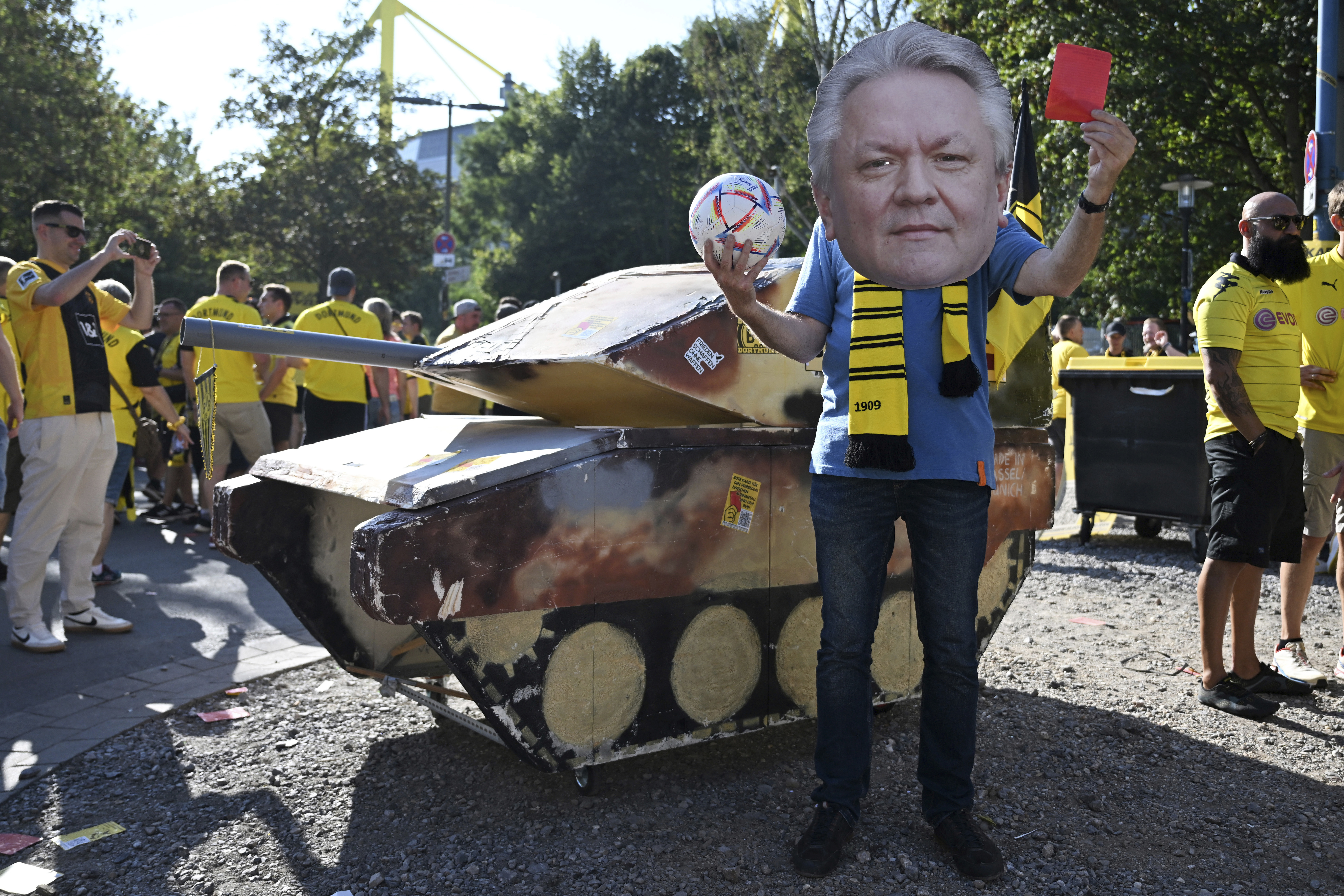 FILE - A dummy tank stands next to an activist wearing a mask with the likeness of Rheinmetall CEO Armin Papperger and holding up a red card ahead of the soccer game between Borussia Dortmund and Eintracht Frankfurt, in Dortmund, Germany, Saturday Aug. 24, 2024. 