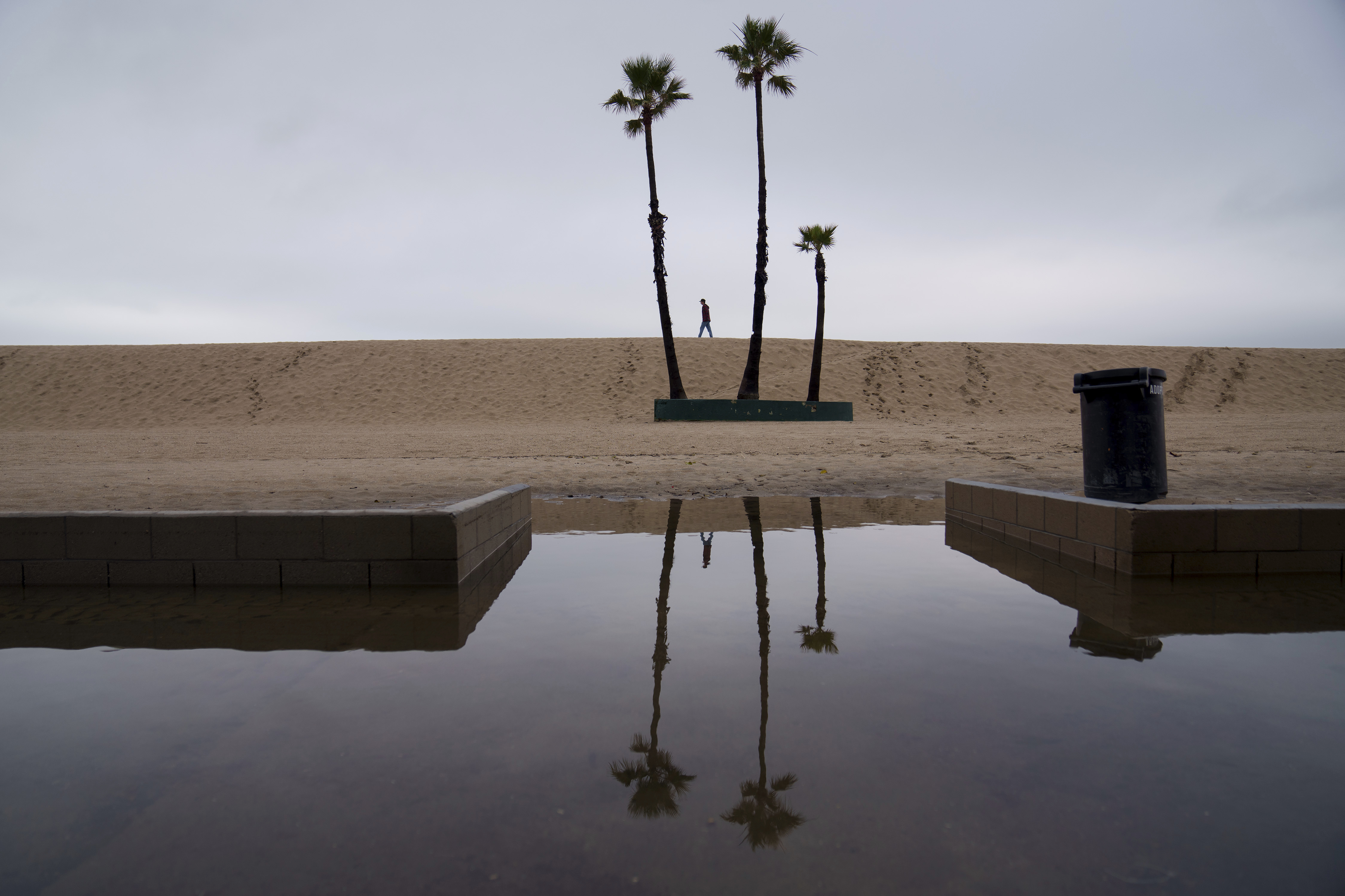 A person walks along the beach with flooding along the boardwalk, Feb. 1, in Seal Beach, Calif. Northern California and the Pacific Northwest are bracing for what is expected to be a powerful storm.