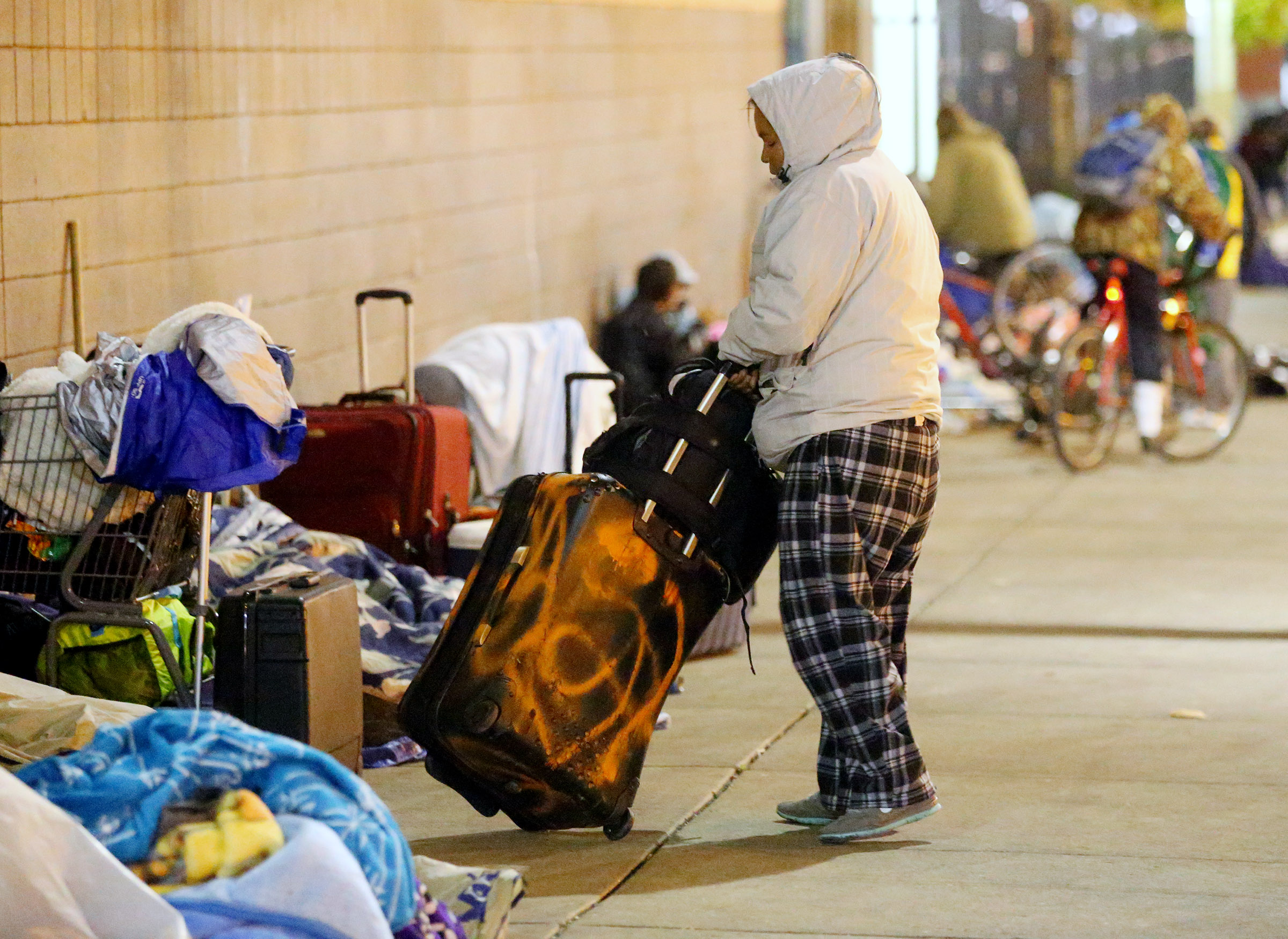 A woman moves a rolling suitcase as she and other folks experiencing homelessness sit outside the winter overflow shelter at St. Vincent de Paul in Salt Lake City on Nov. 16, 2016. In 2024, homelessness prevention leaders prepare for another busy winter.